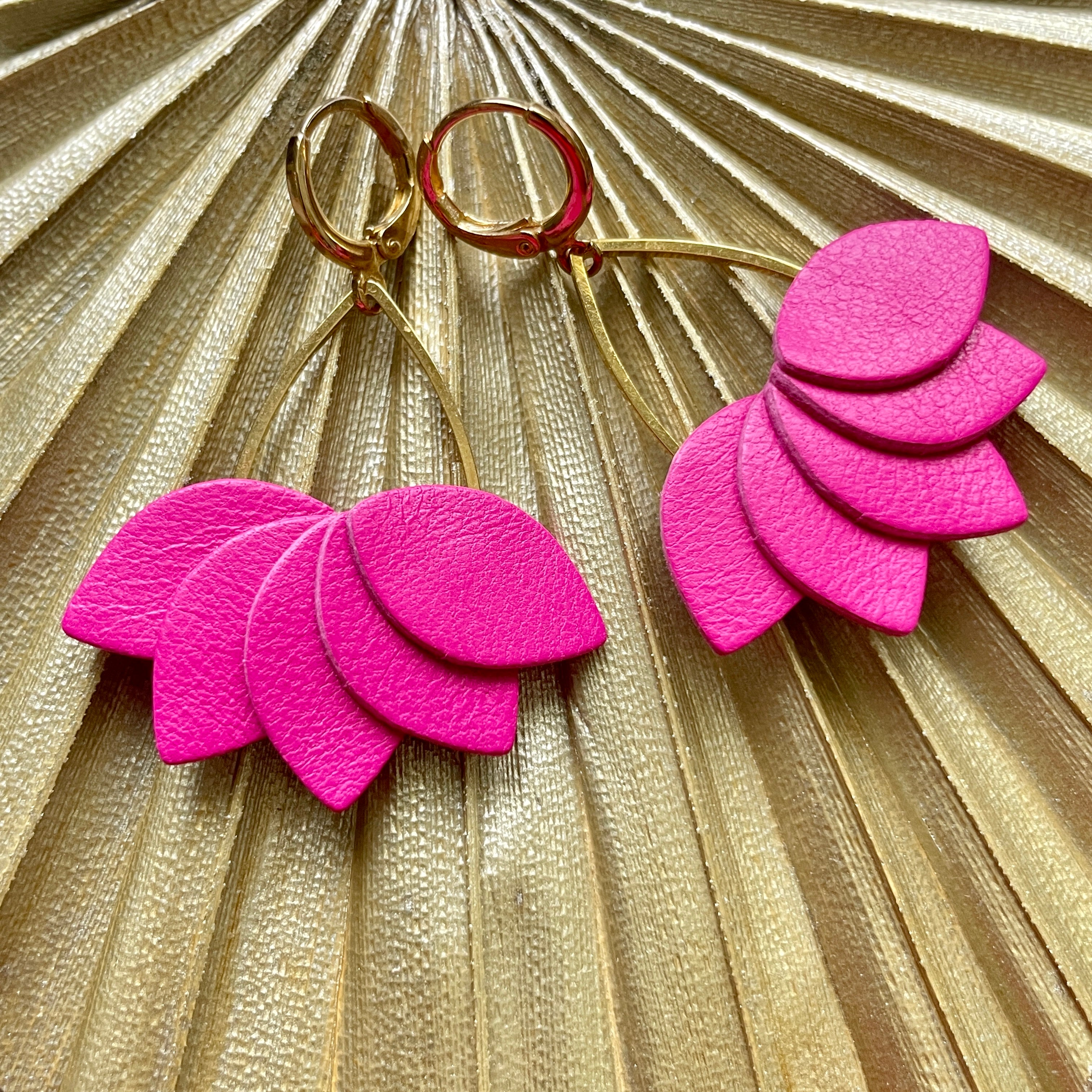 Boucles d'oreilles Nune modÚle Aponi dorées à l'or fin avec pétales de cuir rose flashy en forme de couronne de pétales, sur fond palmier doré