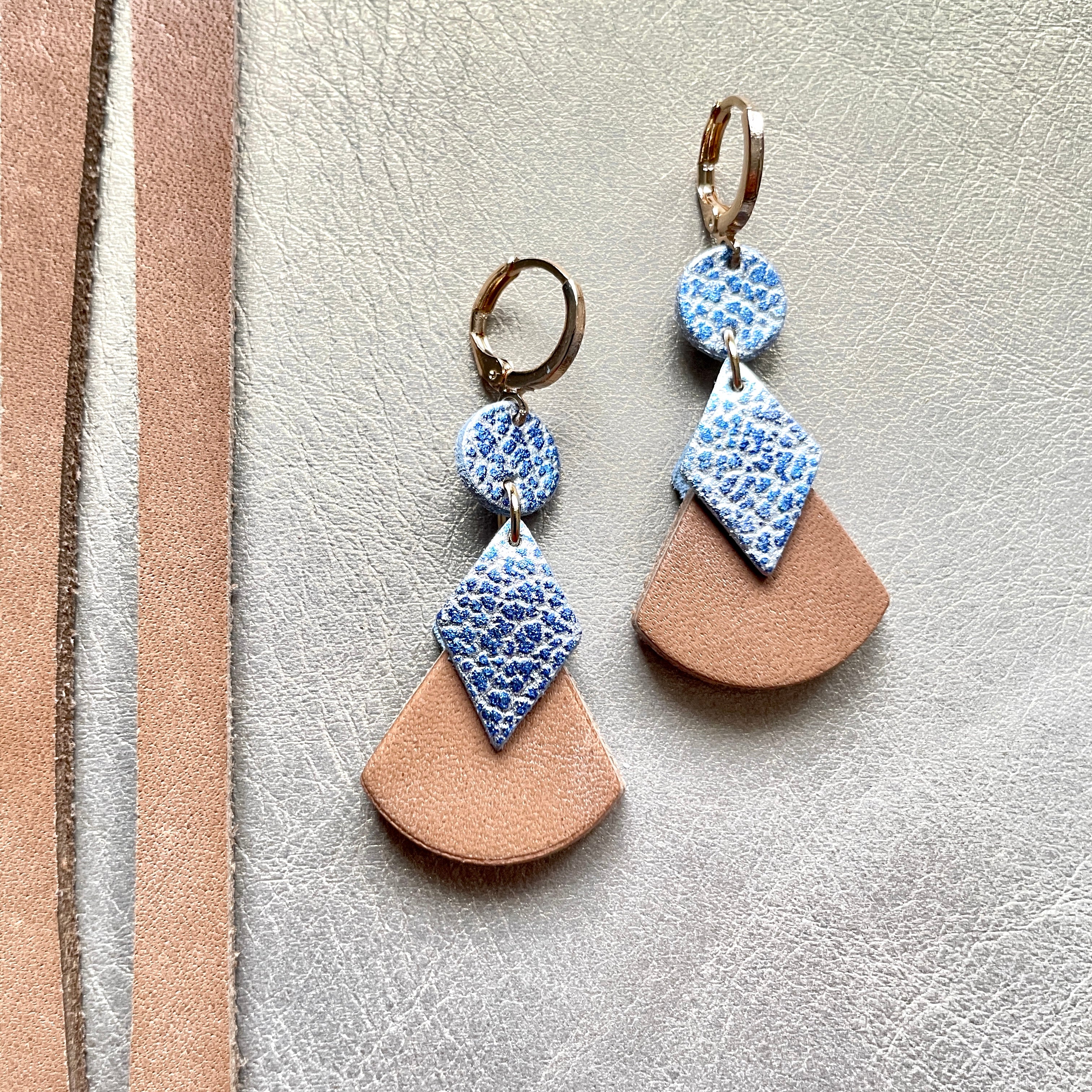 boucles d'oreilles dorées Nune modèle Thémis en cuirs beige amande et bleu ciel métal patiné sur fond gris doré