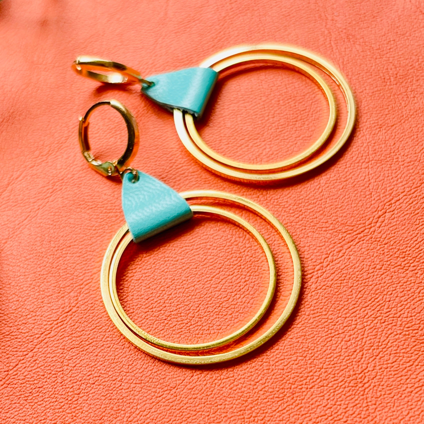 Créoles dorées modèle Vega de la marque Nune, avec une touche de cuir vert menthe, sur fond cuir orange