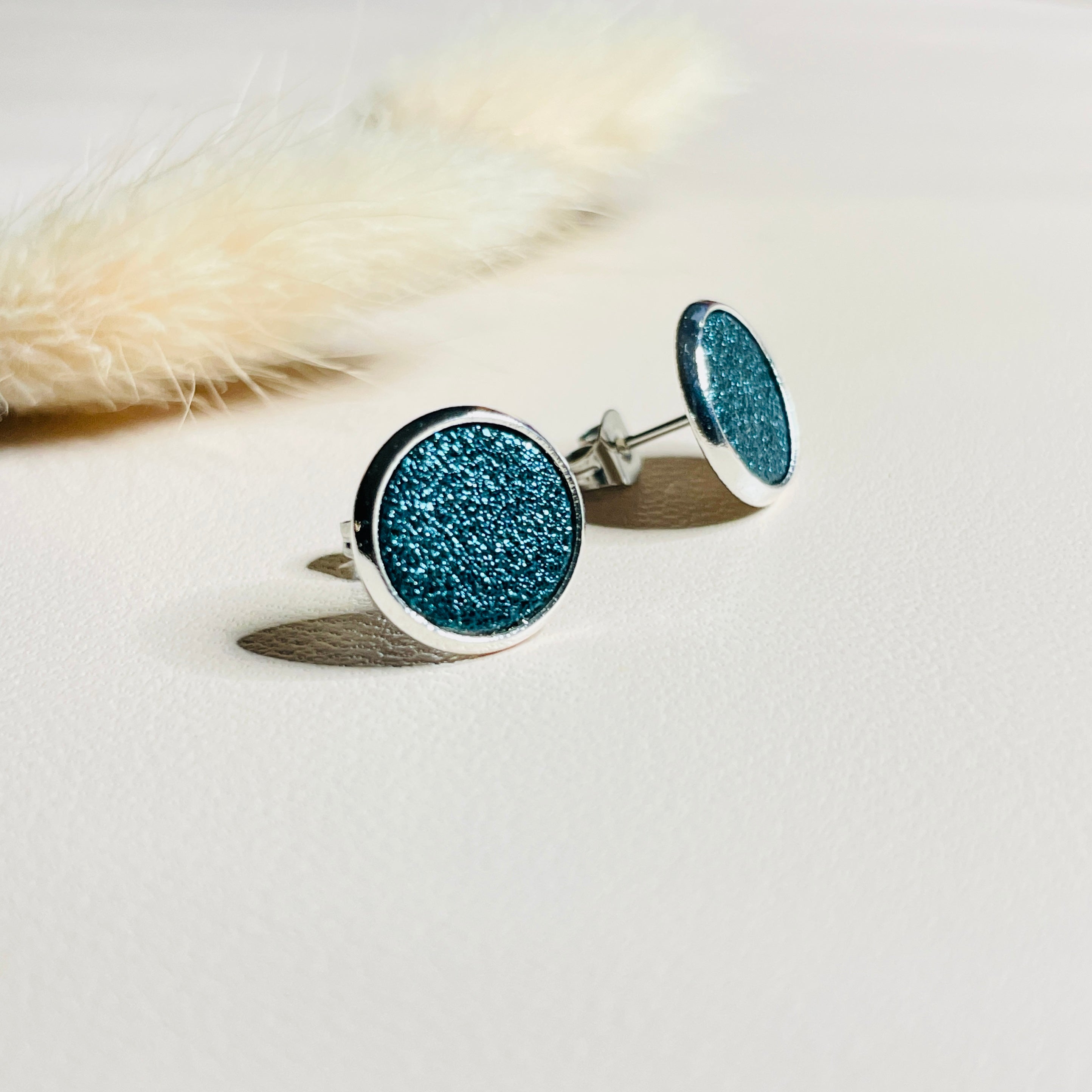 Puces d'oreilles argentées rondes Nune modèle Ilis argenté avec pastilles de cuir saphir pailleté, sur fond de cuir blanc cassé