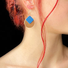 Charger l&#39;image dans la galerie, boucle d&#39;oreille dorée Nune modèle Héra en cuirs beige amande et bleu denim mat portée par un modèle aux cheveux rouges et au teint pâle
