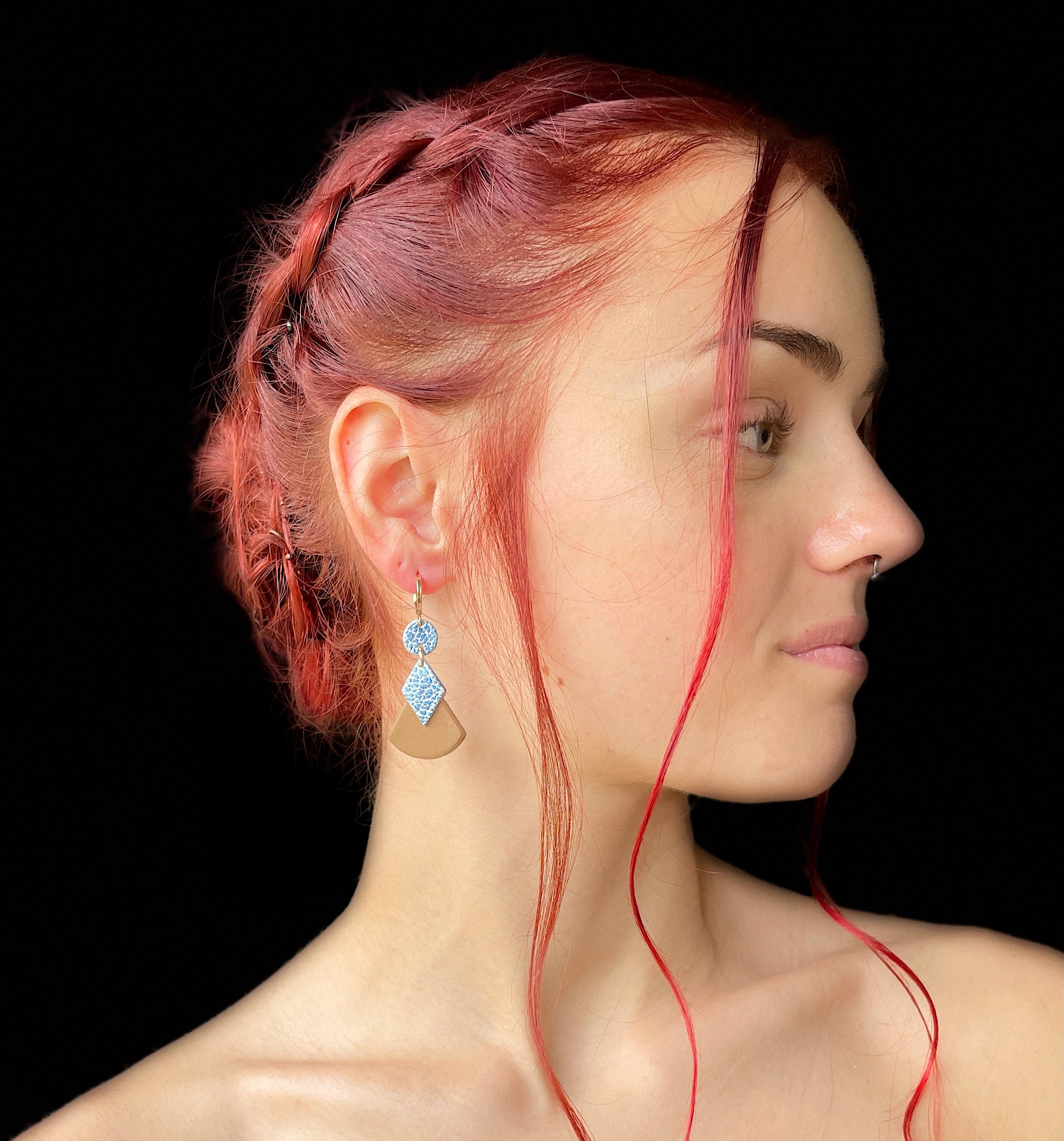 boucle d'oreille dorée Nune modèle Thémis en cuirs beige amande et bleu ciel métal patiné portée par un modèle de profil aux cheveux rouges et au teint pâle