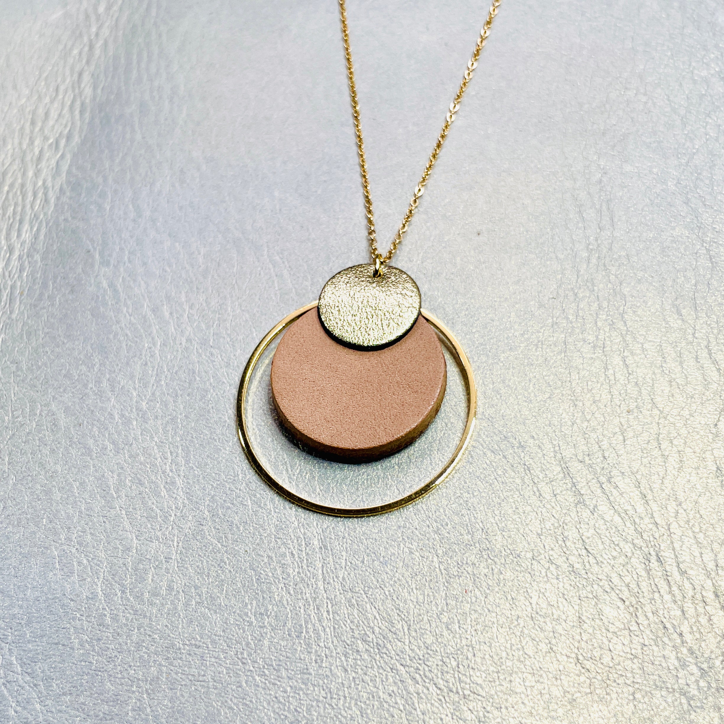 NUNE collier doré fin Danaé avec pendentif rond en cuir recyclé doré satiné, sur fond beige doré. Vue de face