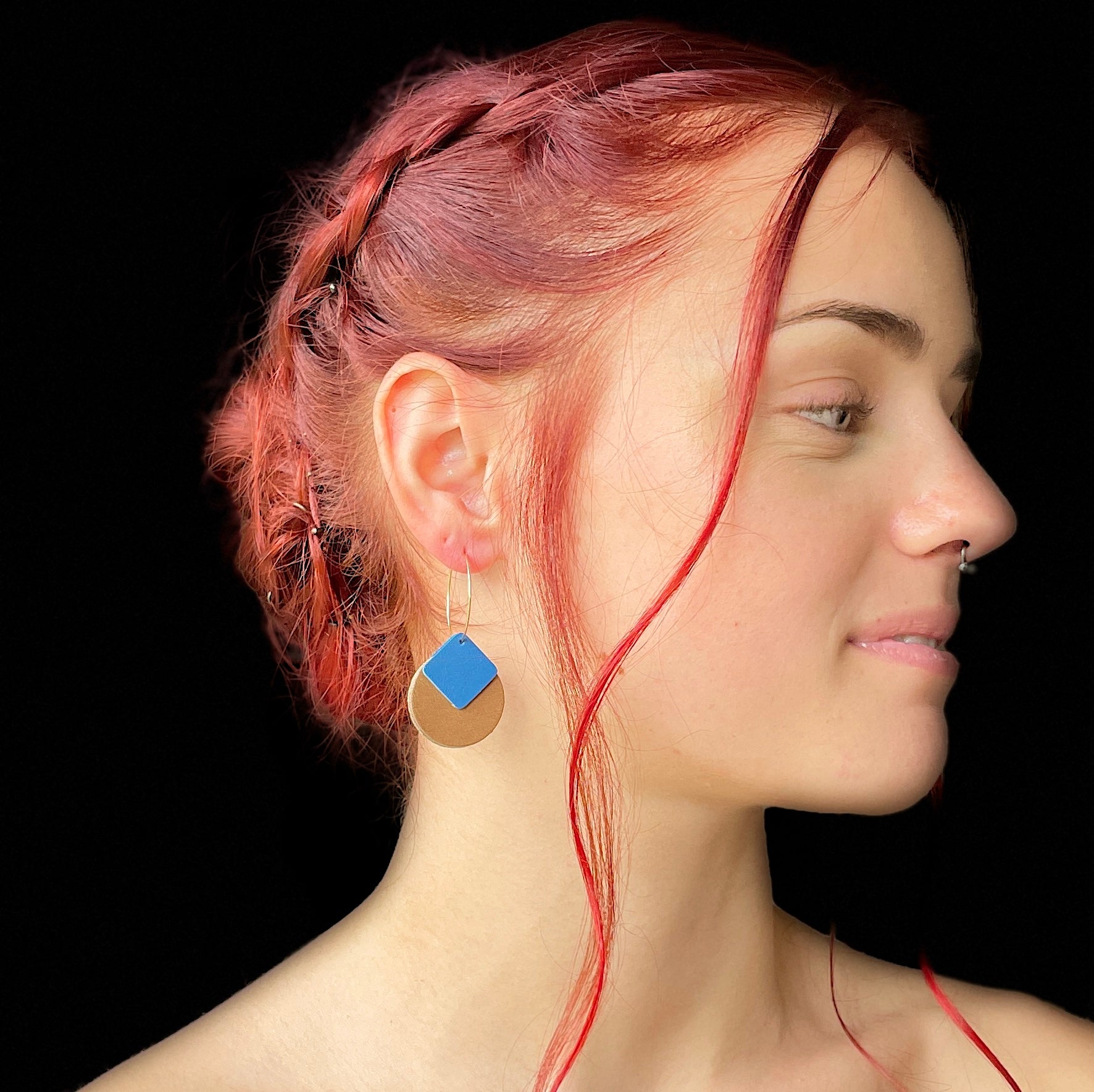 boucle d'oreille dorée Nune modèle Héra en cuirs beige amande et bleu denim mat portée par un modèle de profil aux cheveux rouges et au teint pâle
