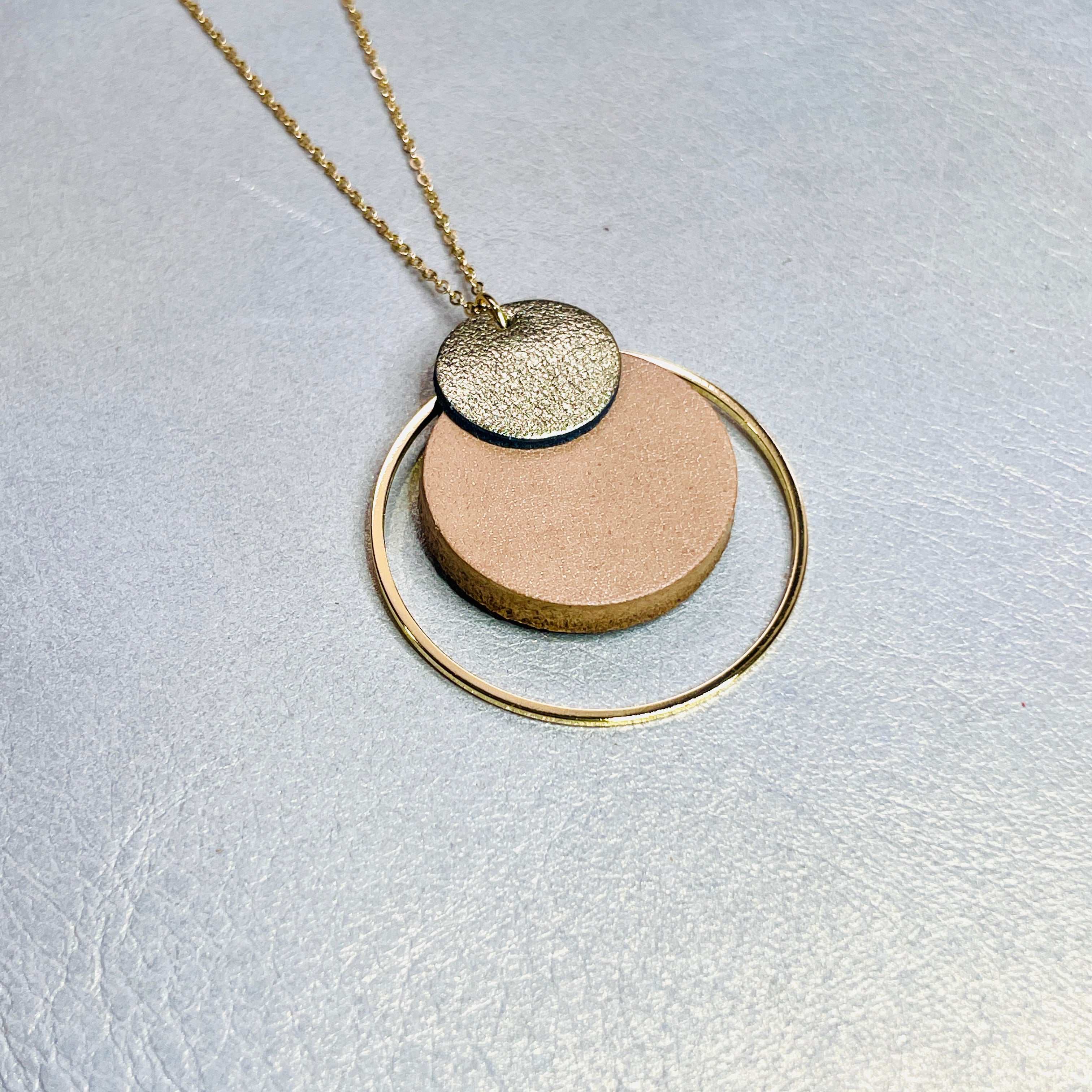 NUNE collier doré fin Danaé avec pendentif rond en cuir recyclé doré satiné, sur fond beige doré. Vue de biais