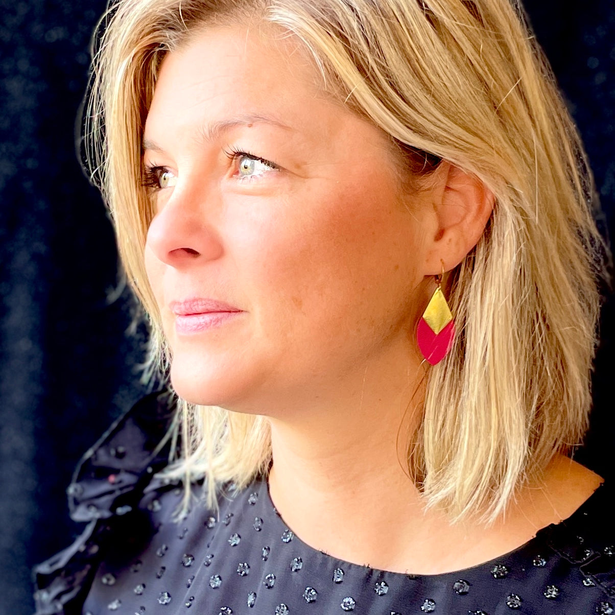 Boucle d'oreille dorée Nune en forme d'olive modèle Olivia en cuir fushia portée par un modèle aux cheveux blonds