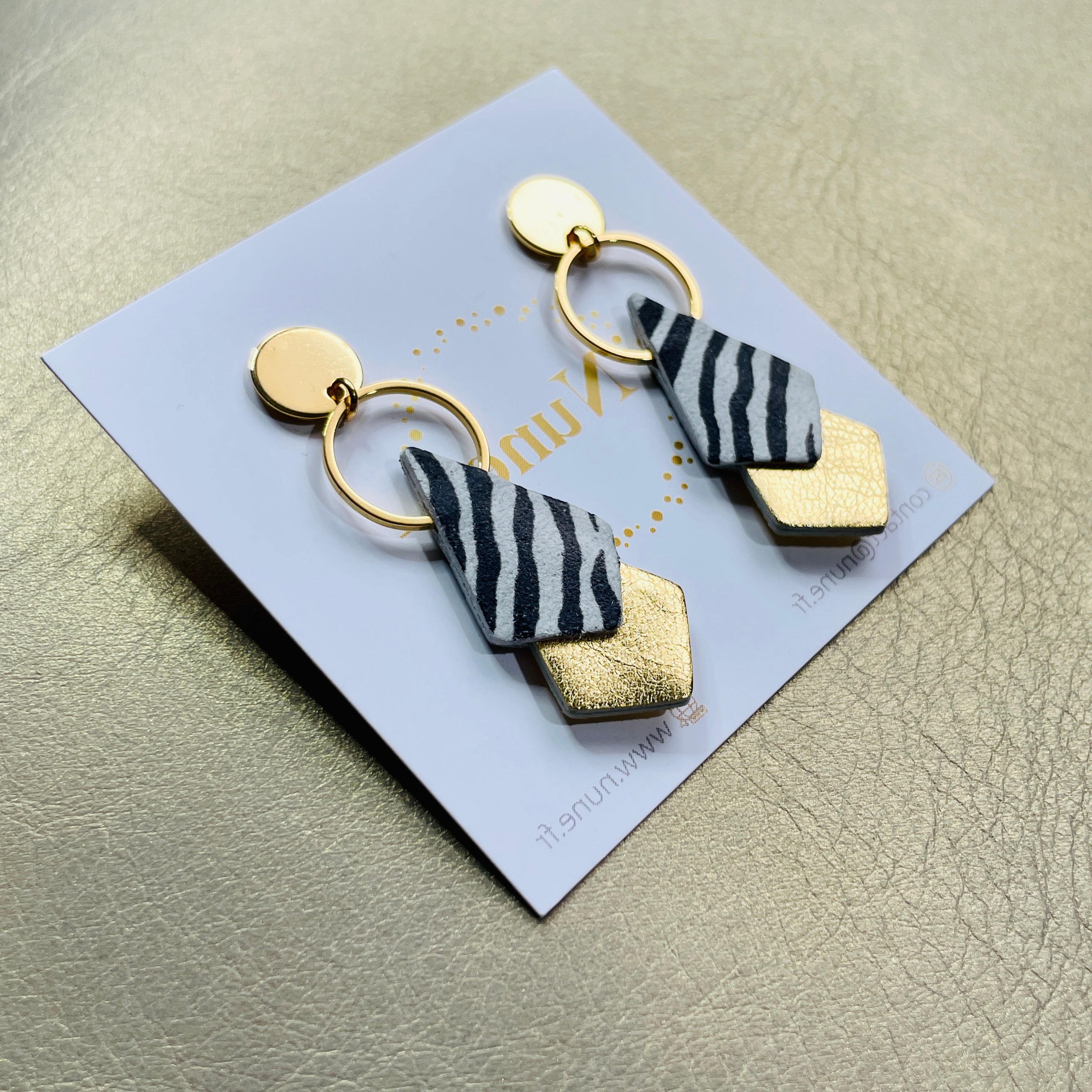 NUNE puces d'oreilles dorées Sagittis, pendentifs en duo de losanges en cuir recyclé zébré noir et doré, sur fond beige doré