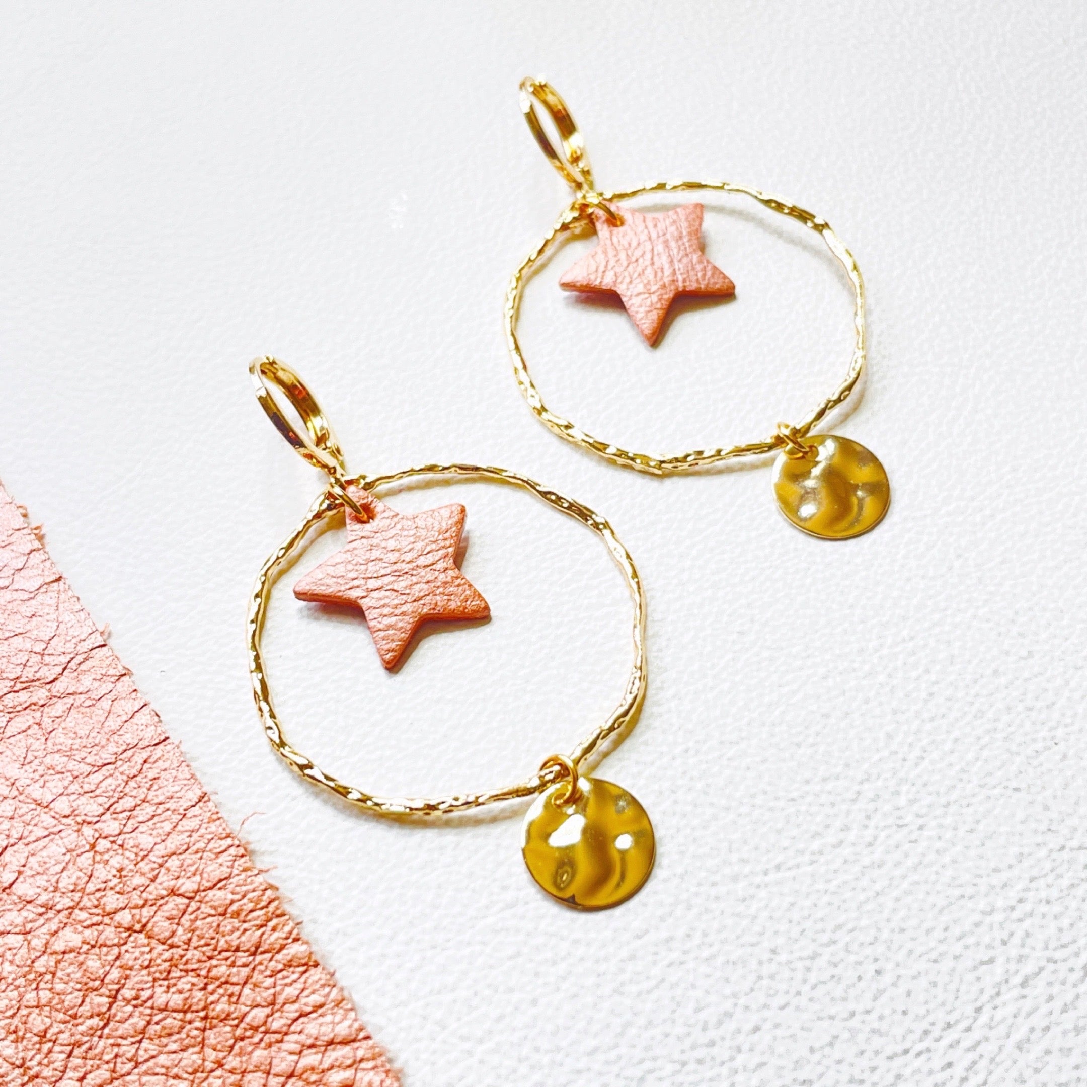 Boucles d'oreilles Nune modèle Naleli dorées à l'or fin de forme créole avec étoile de cuir corail nacré clair, sur fond cuir blanc