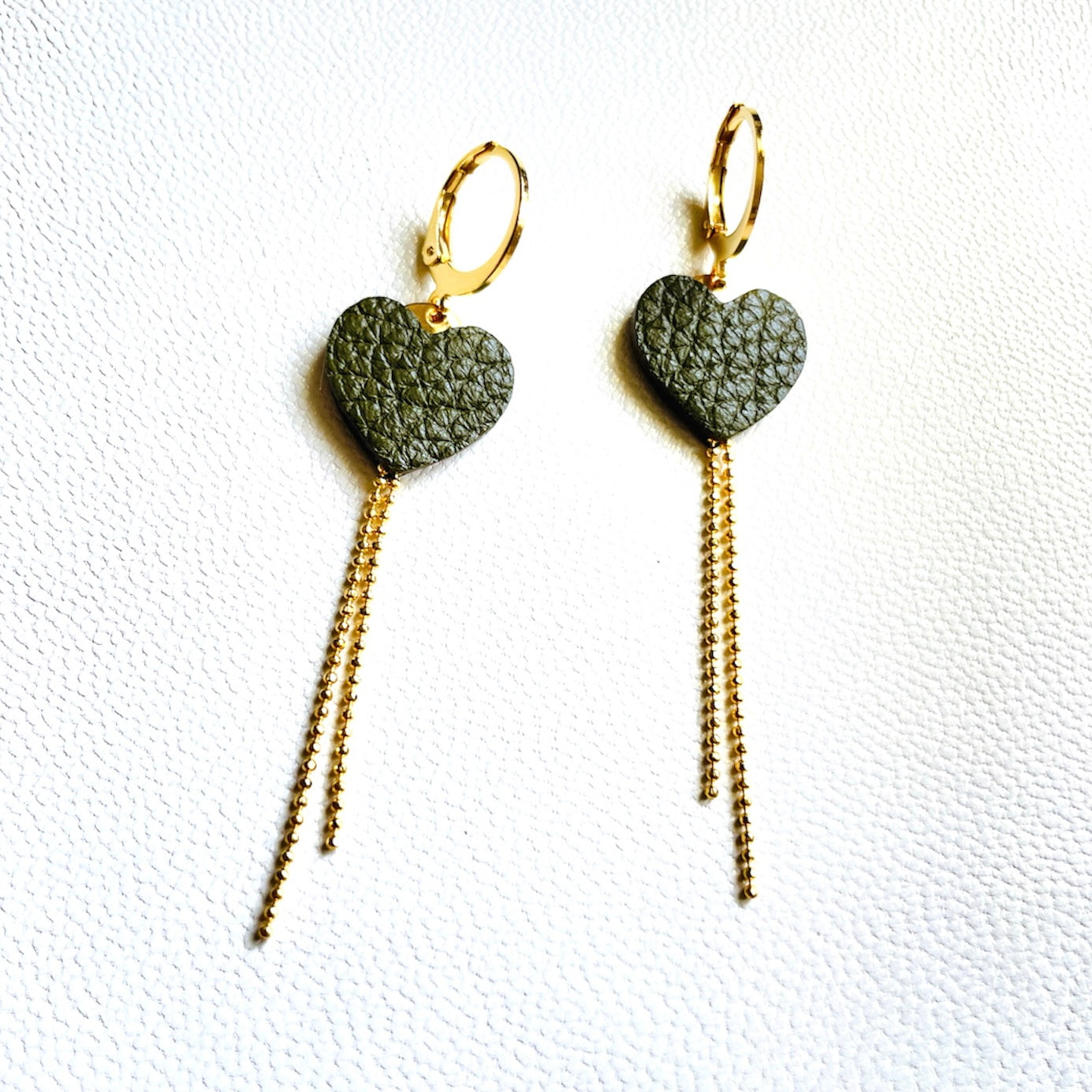 NUNE fines boucles d'oreilles dorées, petits cœurs de cuir recyclé kaki grainé et chaînettes, sur fond gris