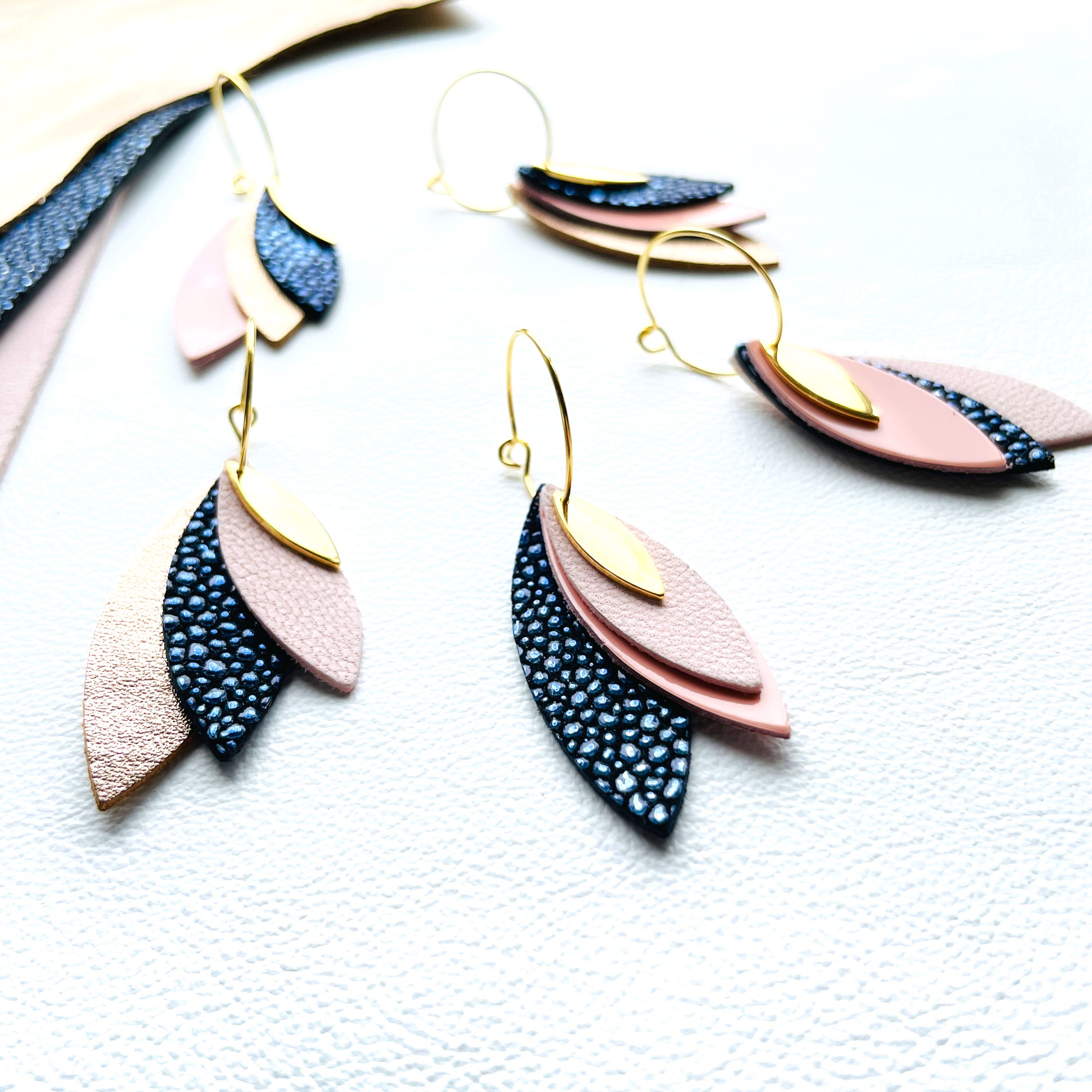 5 déclinaisons de boucles d'oreilles créoles dorées Nune modèle Piume composées d'un trio de cuirs dans les teintes rose et bleu nuit sur fond blanc