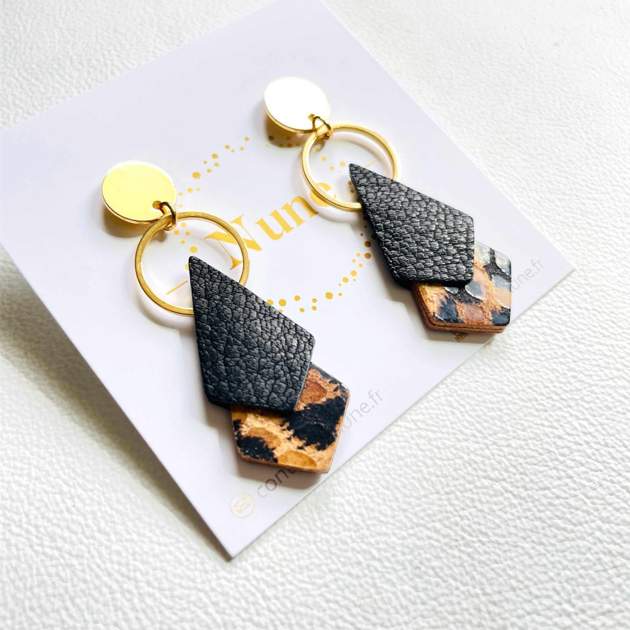 NUNE puces d'oreilles dorées Sagittis, pendentifs en duo de losanges en cuir recyclé noir grainé et façon léopard, sur fond blanc