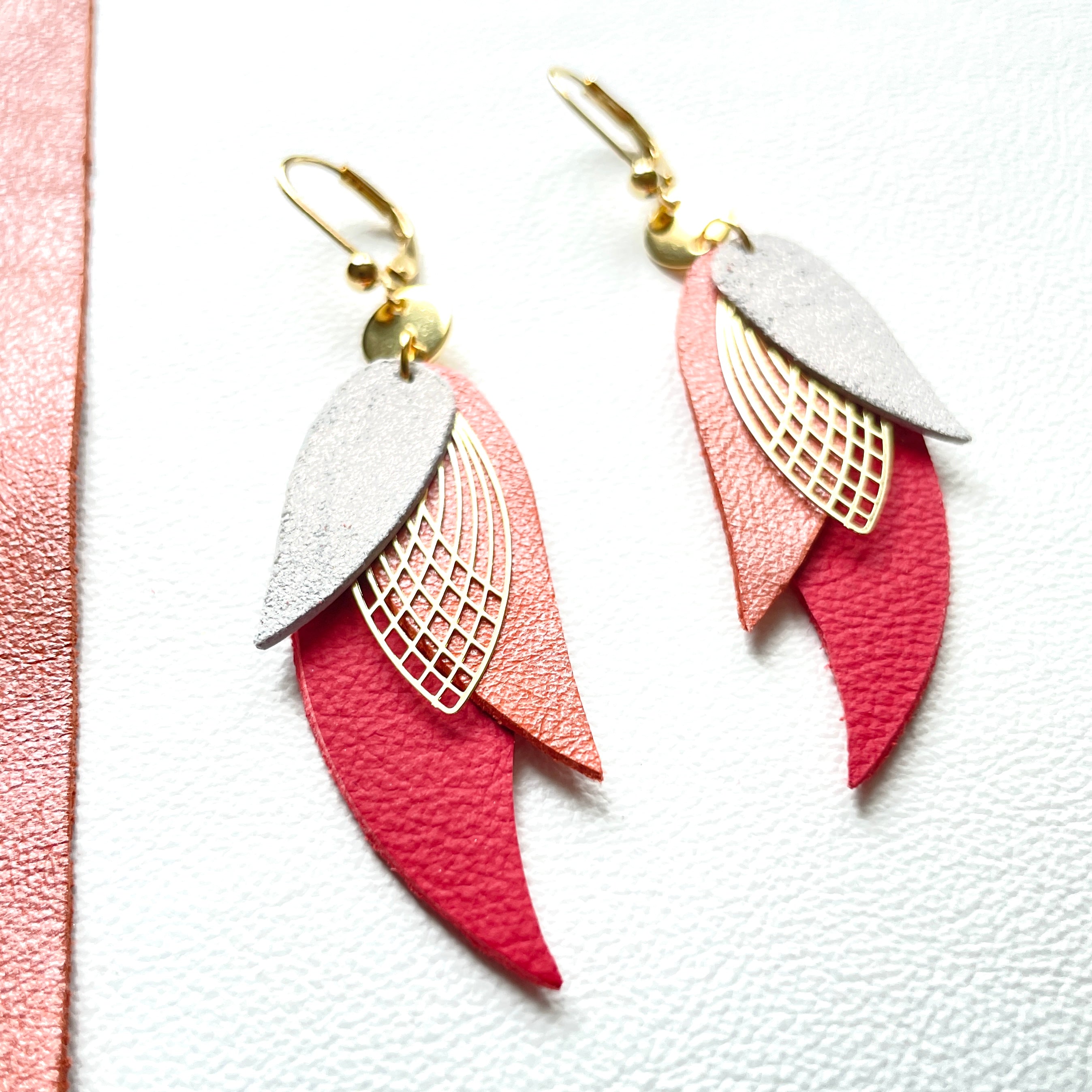 boucles d'oreilles dorées Nune modèle Ara en plumes de cuir gris pailleté, corail nacré et rouge foncé mat sur fond blanc