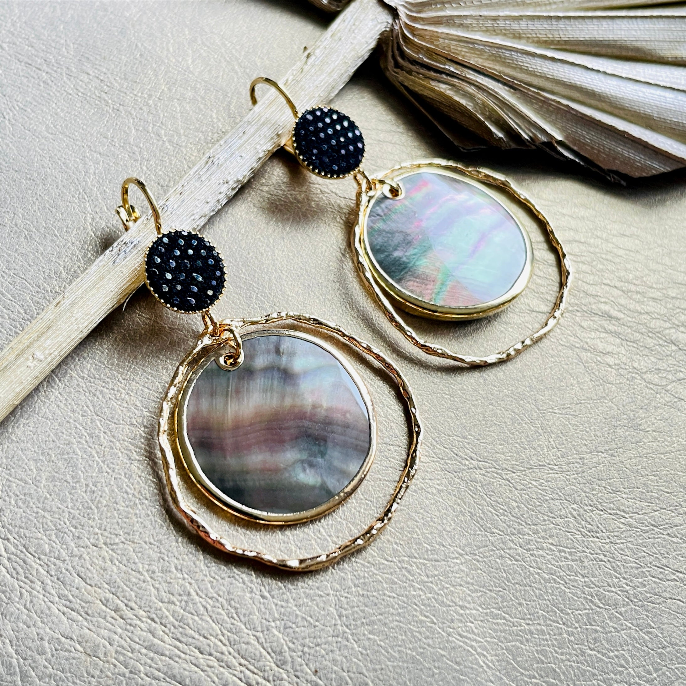 Boucles d'oreilles dorées Nune modèle Bali Créoles Nacre Grise avec du cuir noir grainé irisé sur fond cuir beige doré