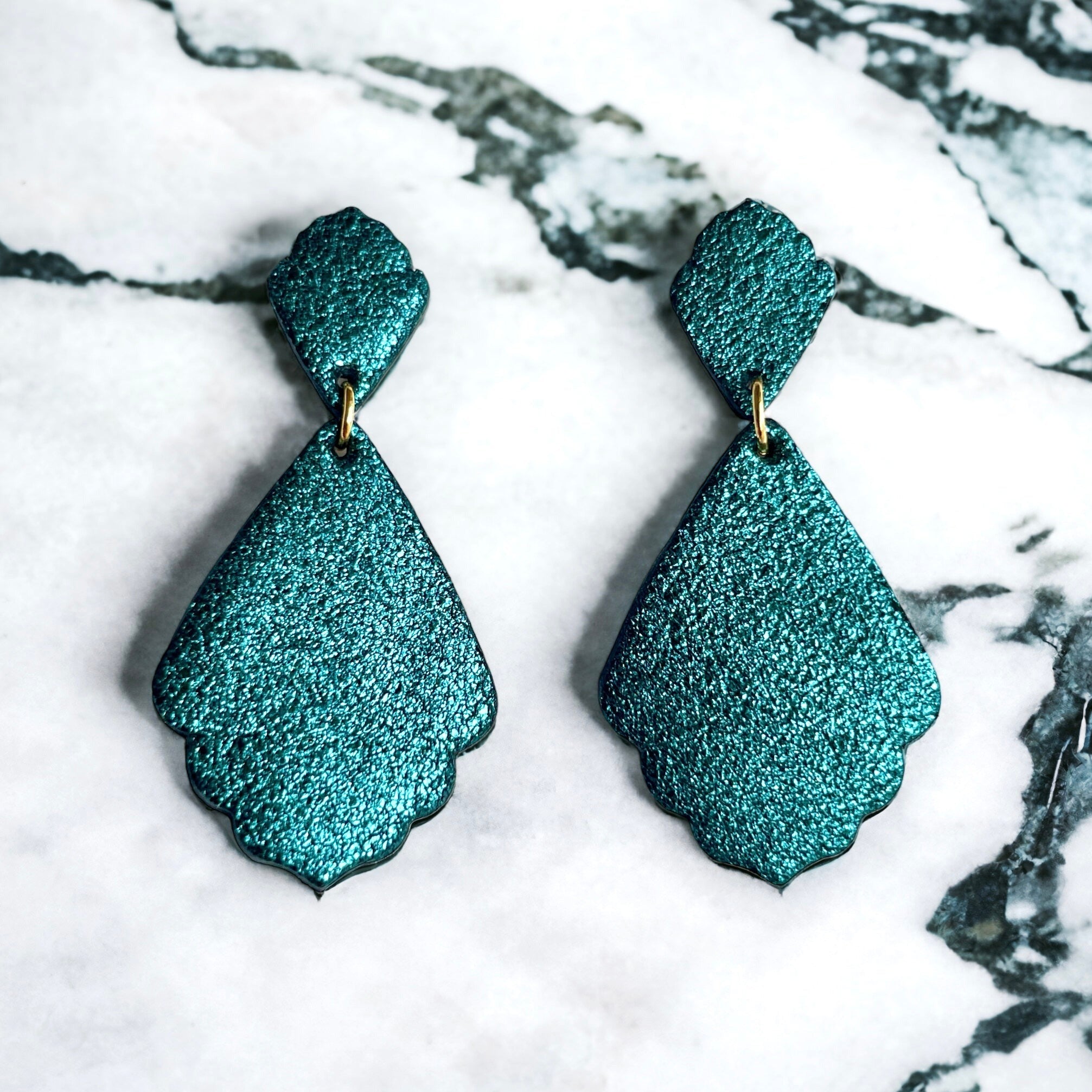 paire de boucles d'oreilles bleu paon pailleté de style rétro baroque, sur fond marbre blanc