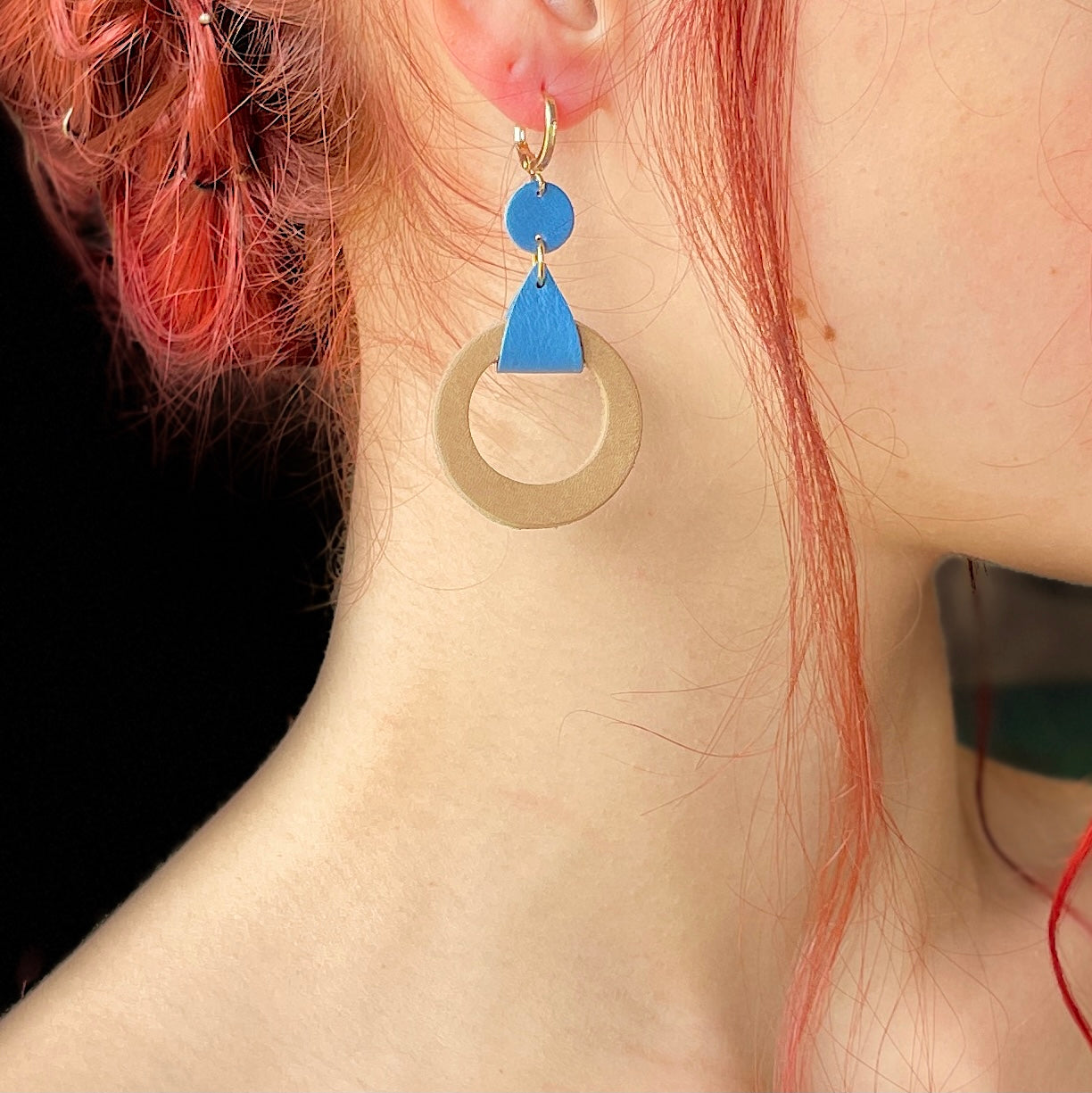 boucle d'oreille dorée Nune modèle Cyllène en cuirs beige amande et bleu denim mat portée par un modèle aux cheveux rouges et au teint pâle