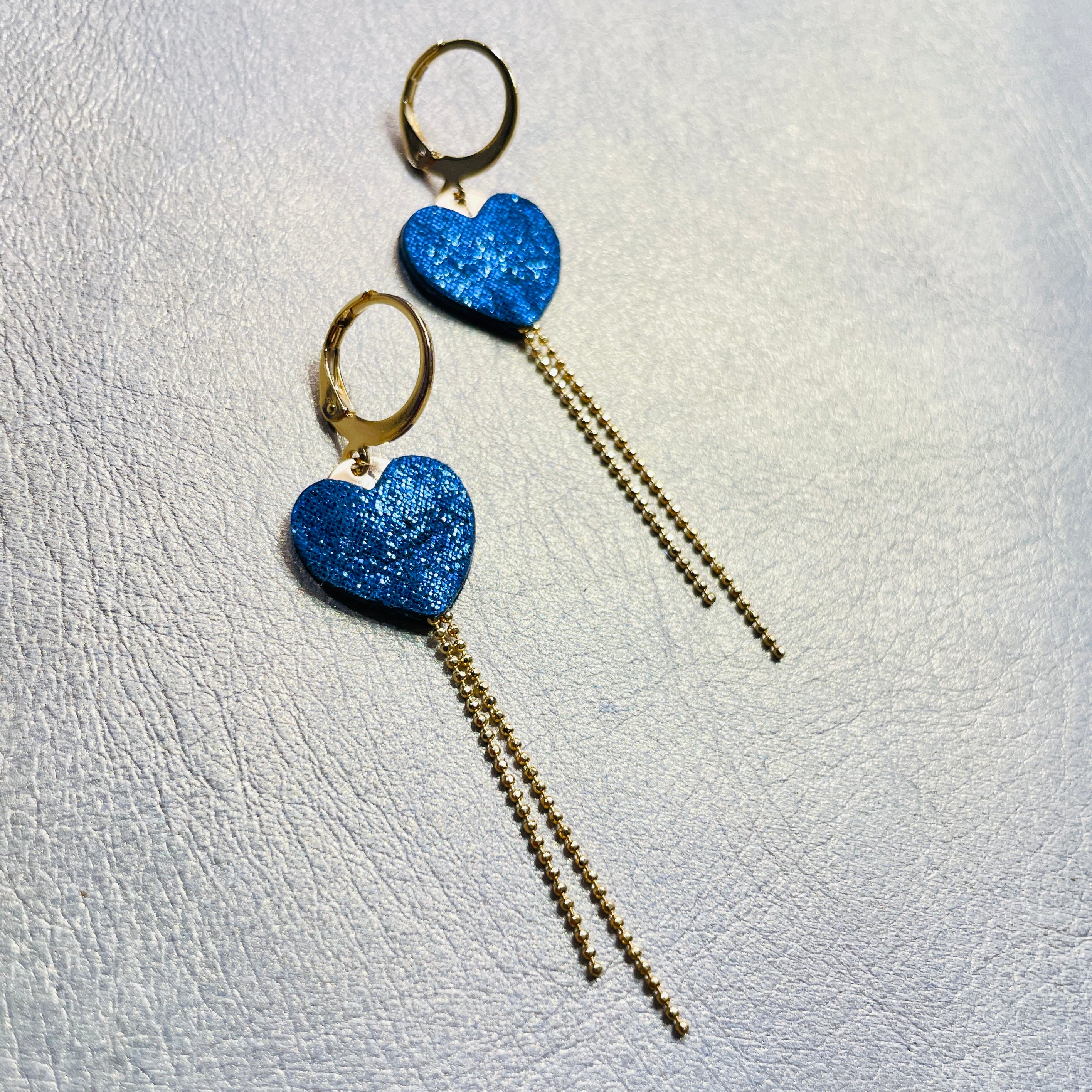 NUNE fines boucles d'oreilles dorées, petits cœurs de cuir recyclé bleu marine pailleté et chaînettes, sur fond gris