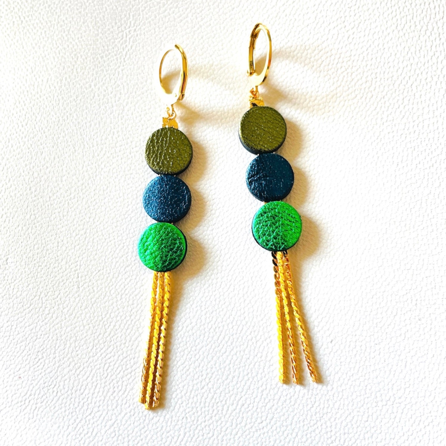 Longues et fines boucles d'oreilles Nune à franges dorées avec 3 petits disques de cuir recyclé kaki métallisé, bleu nuit métallisé et vert métallisé, sur fond blanc. Modèle Janis