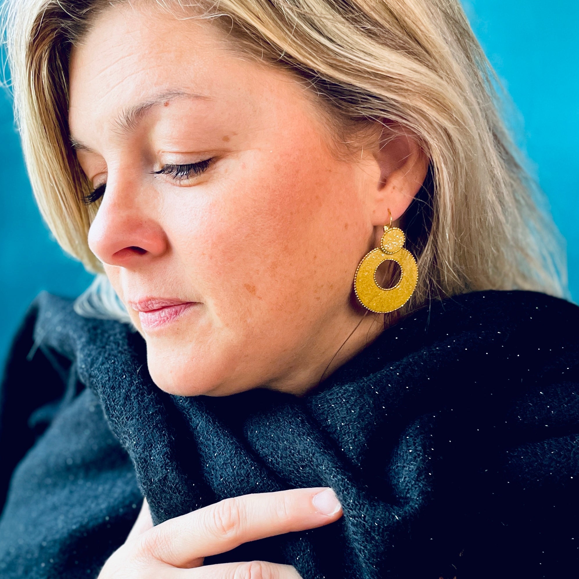 créole ronde Nune modèle Céleste en forme de cercle en cuir safran pailleté argent, cerclée de chaîne dorée, portée par un modèle aux cheveux blonds
