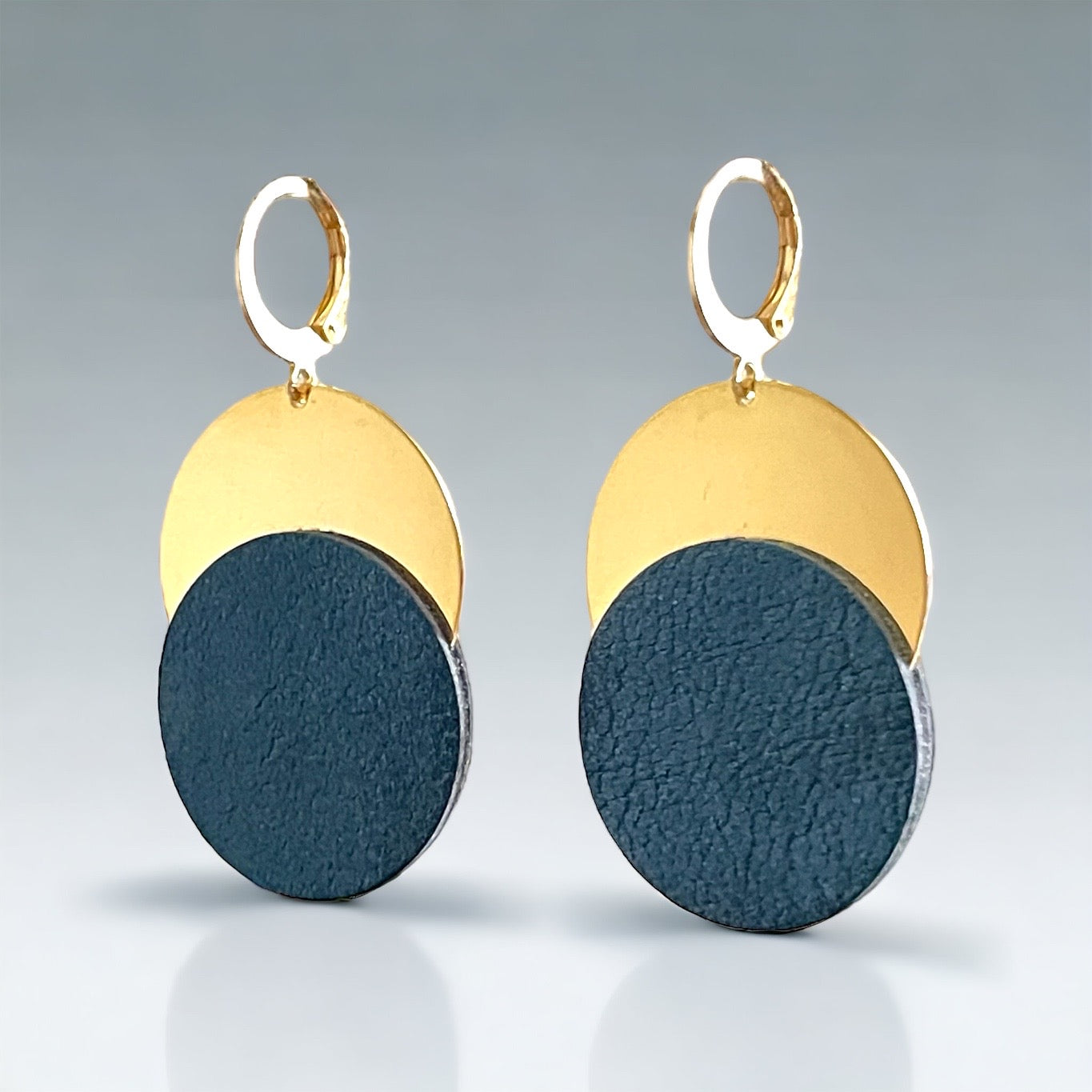 Boucles d'oreilles dorées Nune modèle Eclipse avec disque de cuir bleu nuit sur un disque doré, sur fond clair