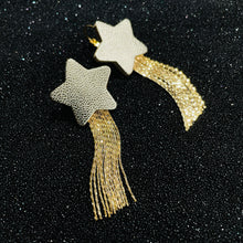 Charger l&#39;image dans la galerie, Nune Boucles d&#39;oreilles légères SuperStella, grandes étoiles en cuir argenté recyclé et leurs longues et fines chaînettes dorées, sur fond noir grainé pailleté vues de dessus
