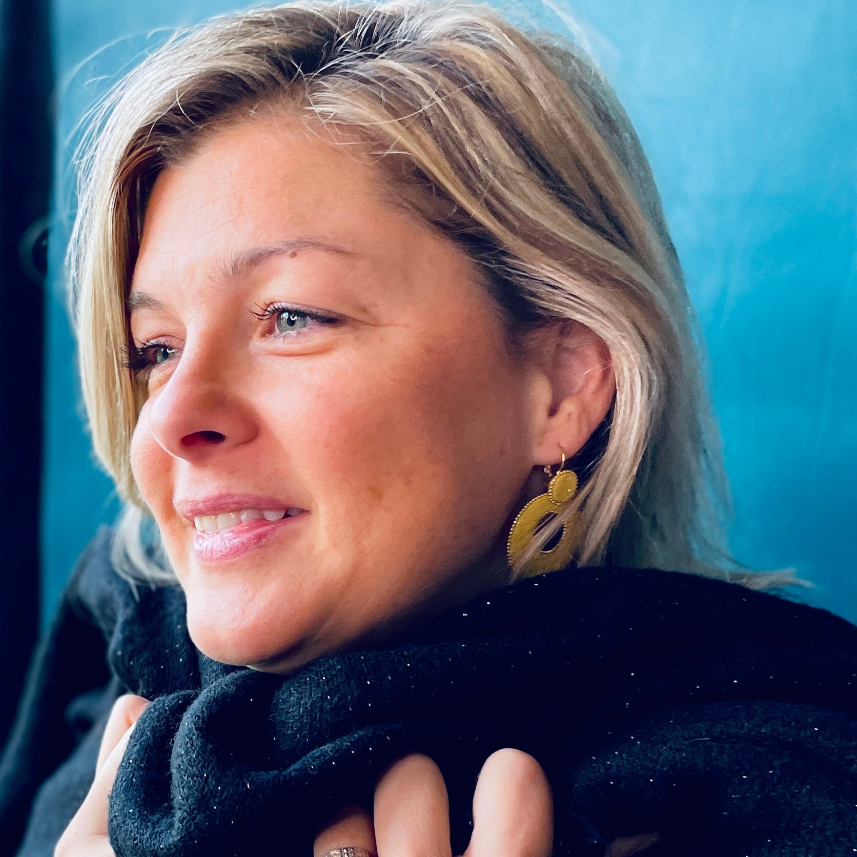 boucle d'oreille créole Nune modèle Céleste en forme de cercle en cuir safran pailleté argent, cerclée de chaîne dorée, portée par un modèle aux cheveux blonds