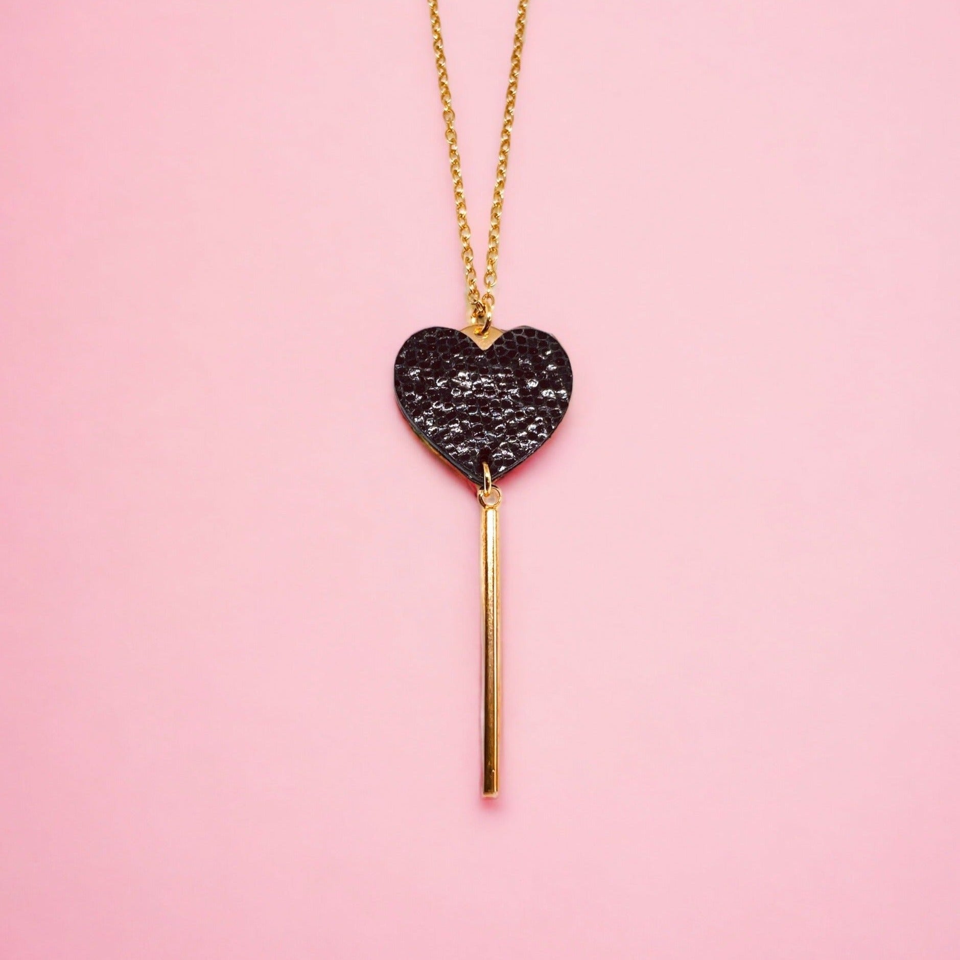 NUNE collier doré Félicie en forme de clé des cœurs cœur en cuir recyclé noir brillant façon serpent sur fond rose pastel