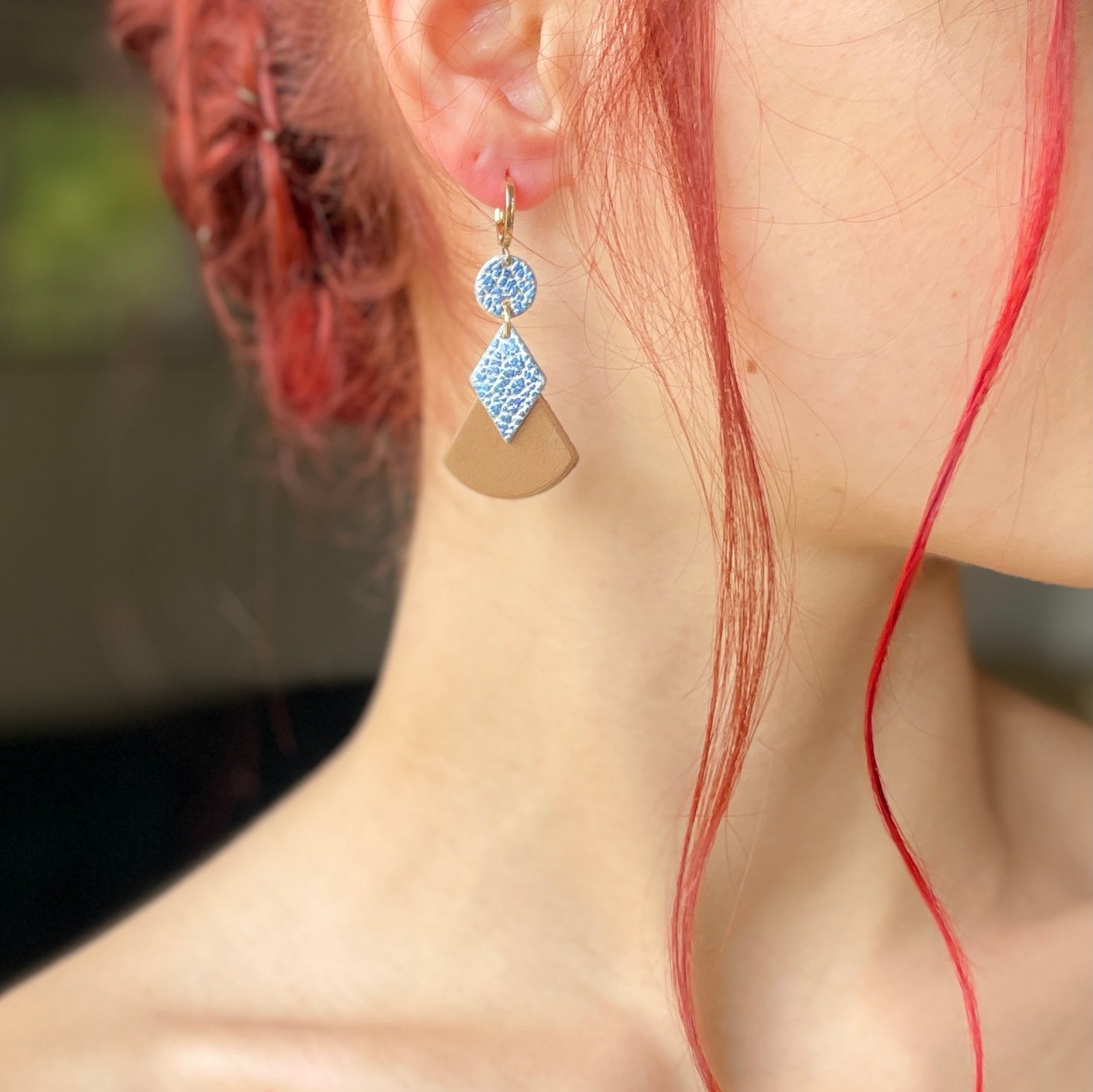 boucle d'oreille dorée Nune modèle Thémis en cuirs beige amande et bleu ciel métal patiné portée par un modèle aux cheveux rouges et au teint pâle