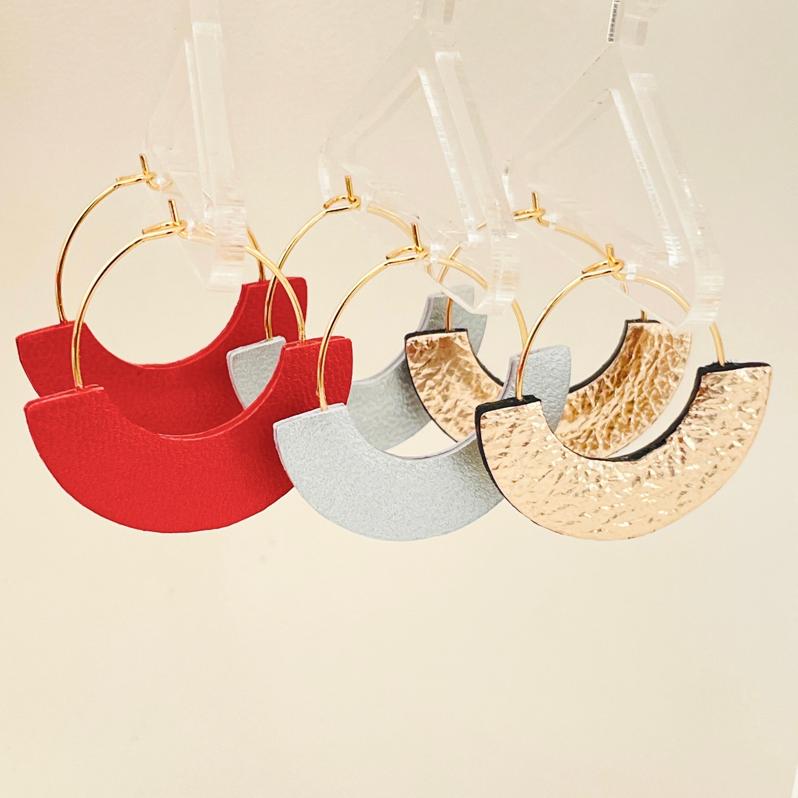 3 paires de boucles créoles Nune modèle Mezzaluna dorées en forme de demi-lunes en cuirs recyclés coquelicot nacré, gris métallisé et doré clair froissé