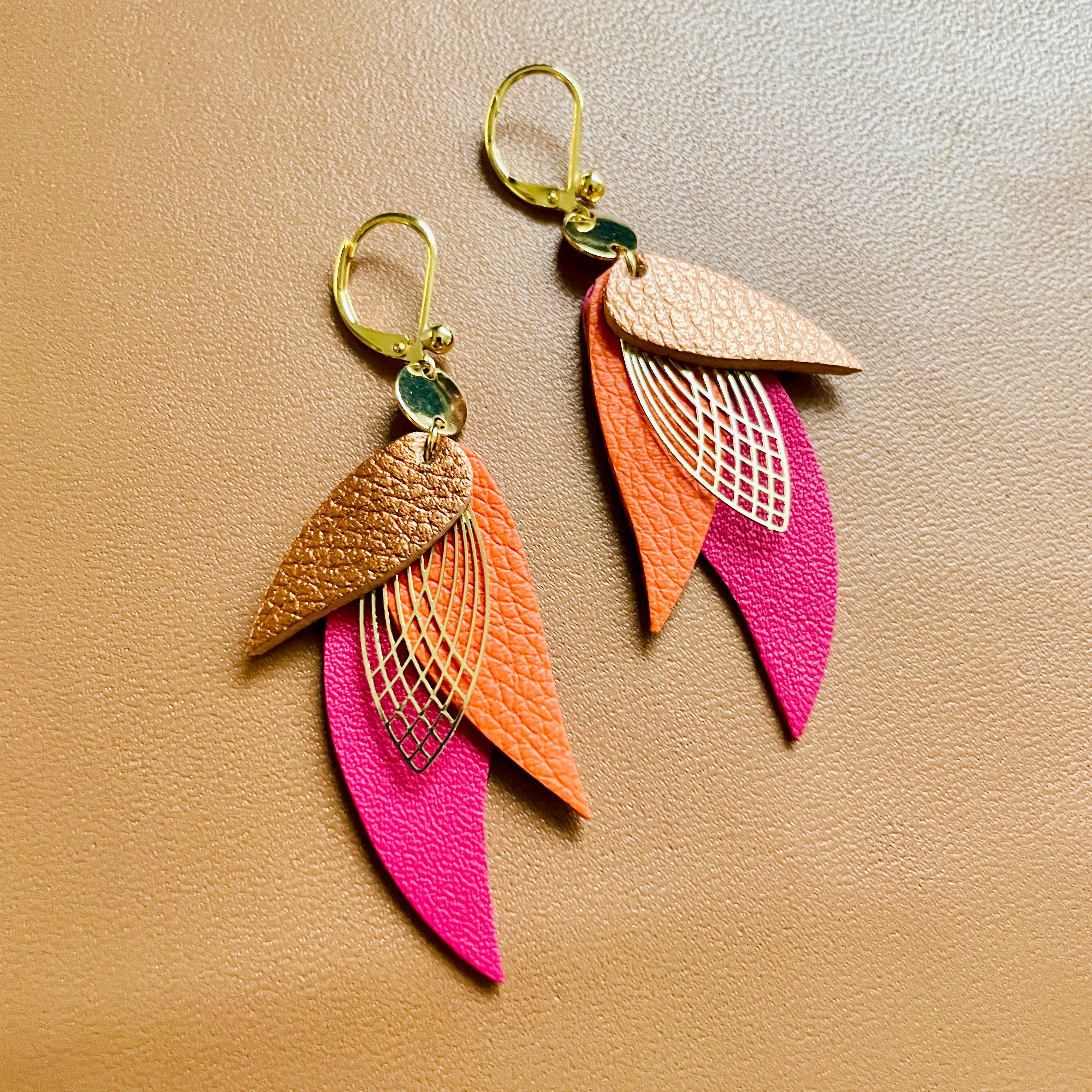 boucles d'oreilles dorées Nune modèle Ara en plumes de cuirs cuivre, carotte grainé et fushia sur donc beige