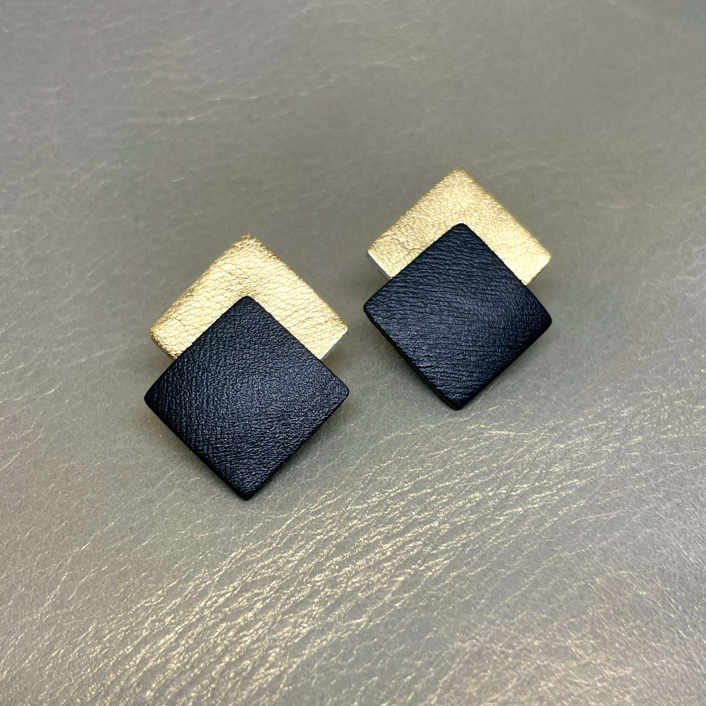NUNE boucles d'oreilles puces Adalis, duo de losanges en cuir recyclé noir satiné et doré clair, sur fond gris irisé