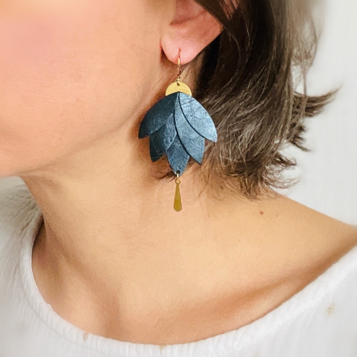 Boucles d'oreilles dorées pendantes Nune modèle Nymphéa en cuir bleu nuit métallisé, portées à l'oreille