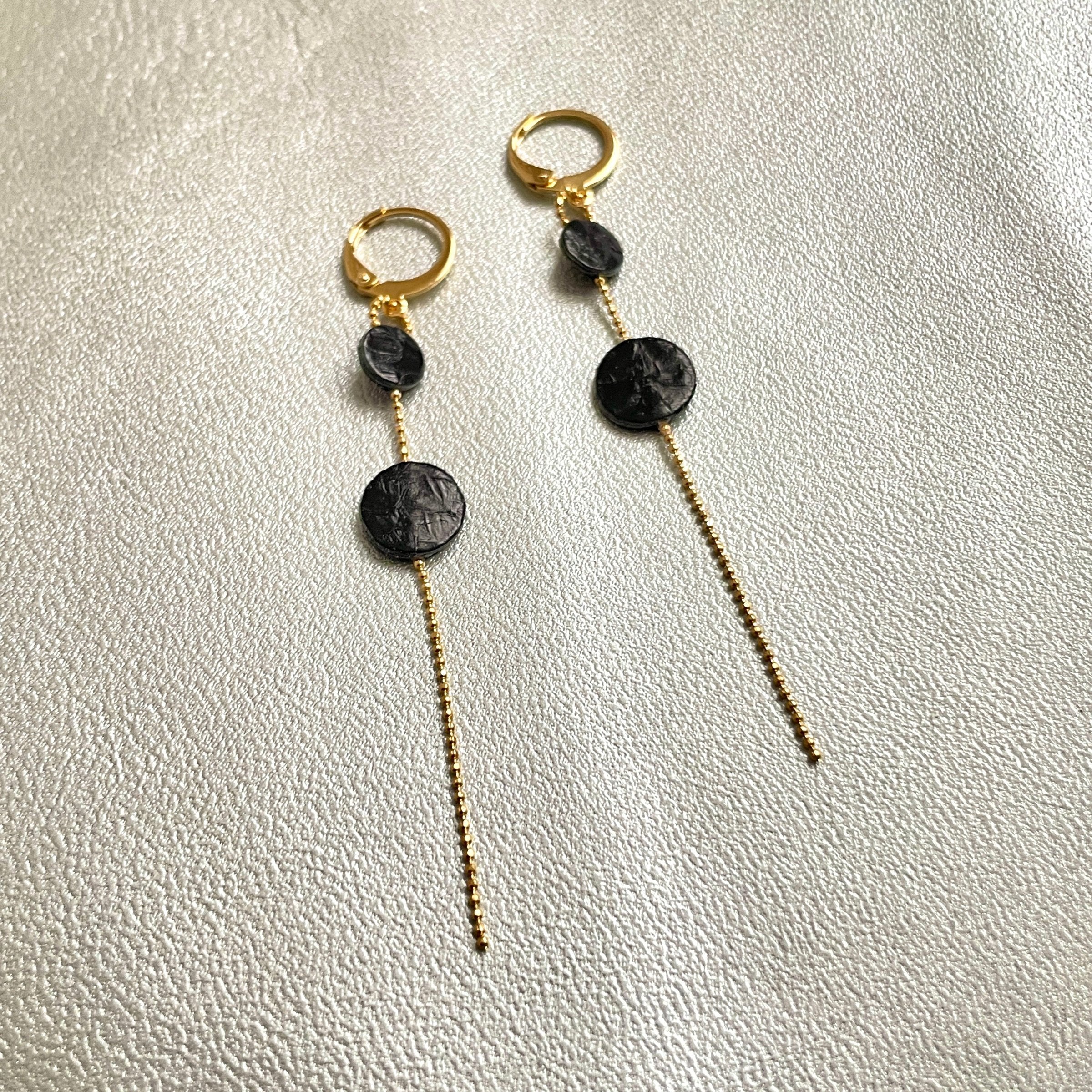 Fines boucles d'oreilles Lyre de Nune, dorées à l'or fin avec petites pastilles de cuir marin, cuir de poisson saumon noir d'encre sur chaînette dorée, sur fond gris argenté