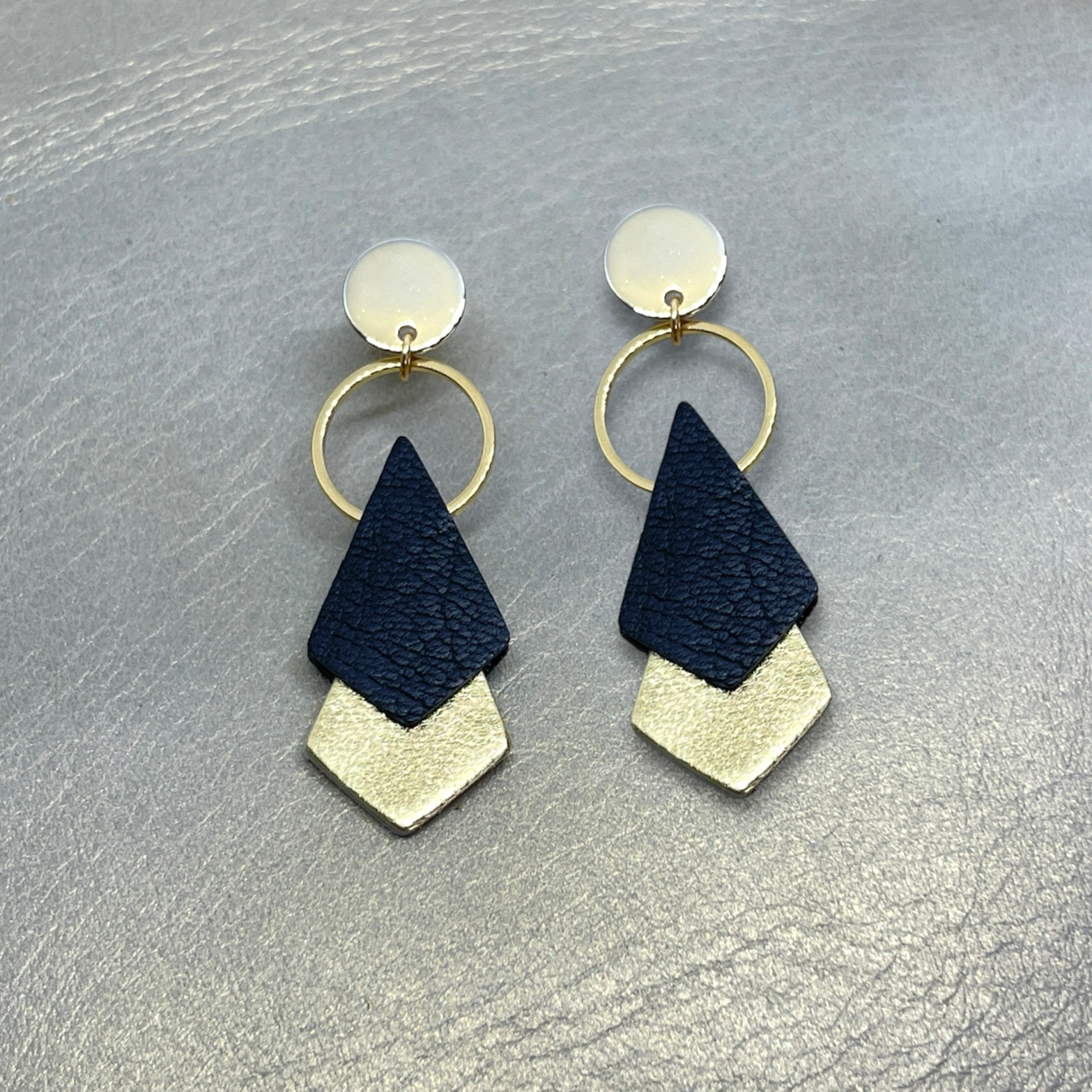 NUNE puces d'oreilles dorées Sagittis, pendentifs en duo de losanges en cuir recyclé noir et doré, sur fond beige doré