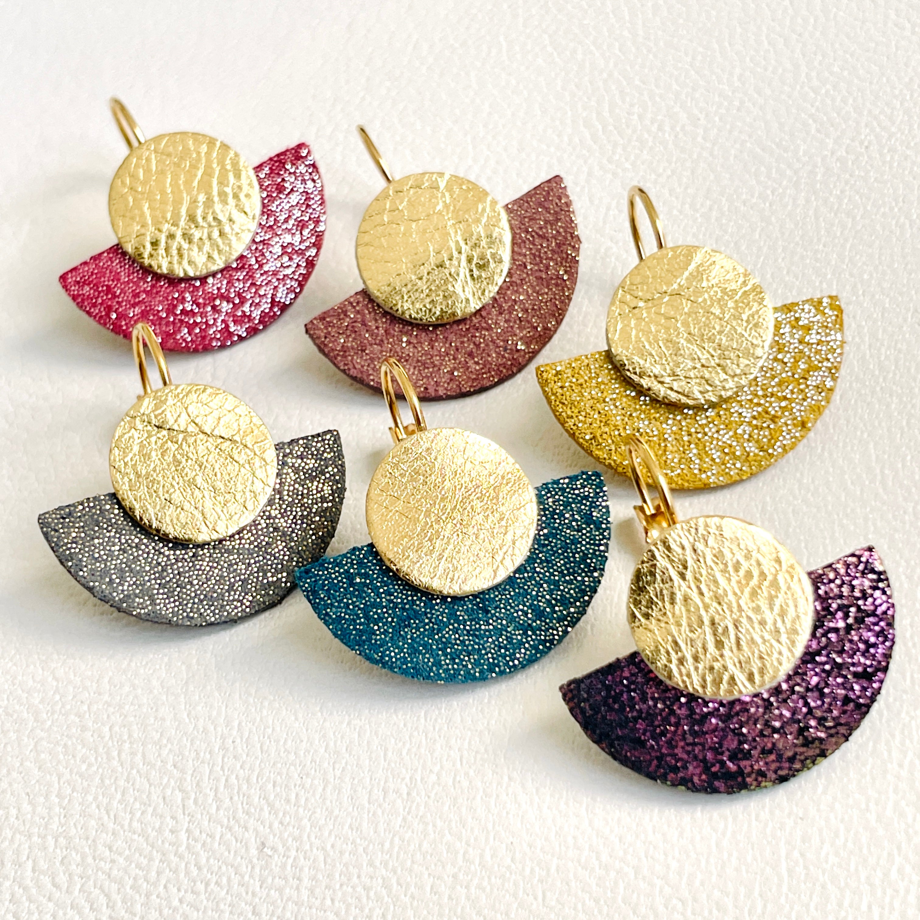 NUNE 6 boucles d'oreilles dorées en forme de demi-lune en 6 teintes de cuirs pailletés et or recyclés, sur fond blanc. Modèle Téthys
