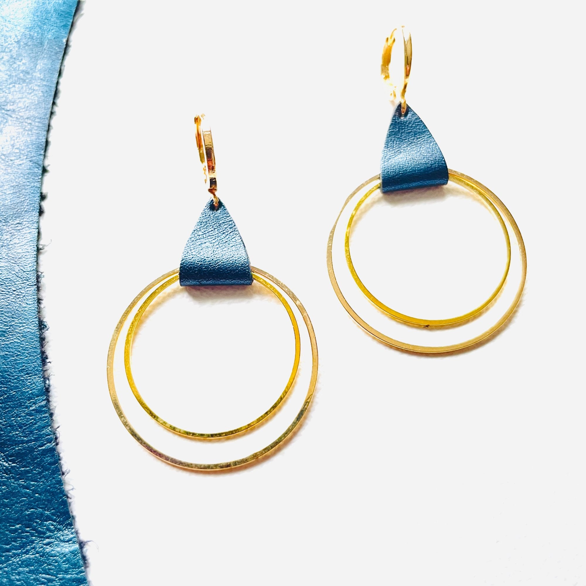 Créoles dorées du modèle Vega de la marque Nune, avec une touche de cuir bleu nuit métallisé, présentées sur fond blanc avec une chute de cuir de la même teinte