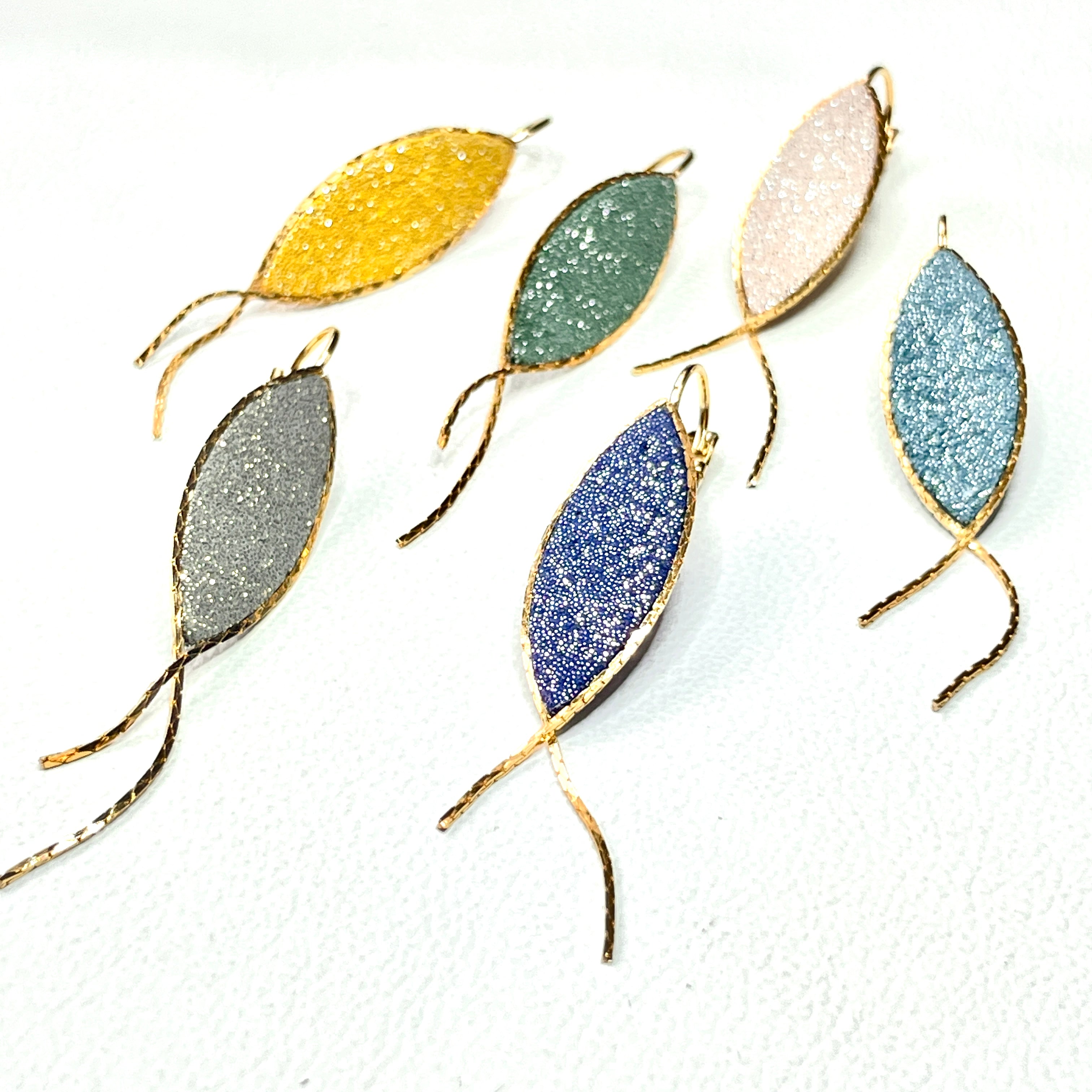 Boucles d'oreilles Nune modèle Nayati en forme de fins poissons dans 6 coloris de cuirs pailletés, cerclés de chaîne dorée, vues de dessus, sur fond blanc