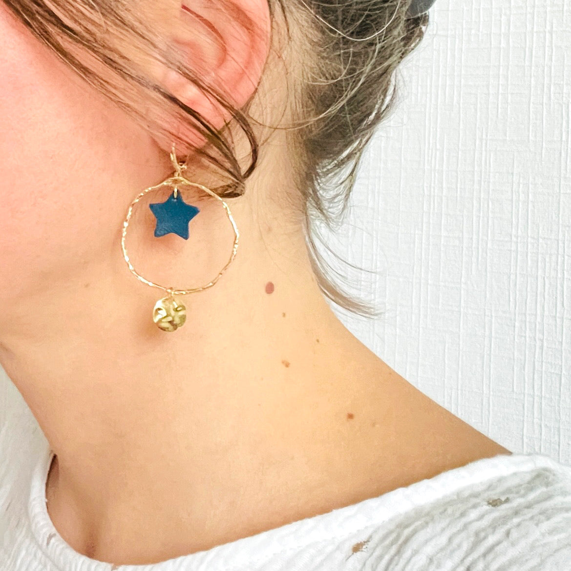 Boucle d'oreille créole dorée martelée Nune modèle Naleli avec une petite étoile en cuir bleu marine portée à l'oreille par une jeune femme