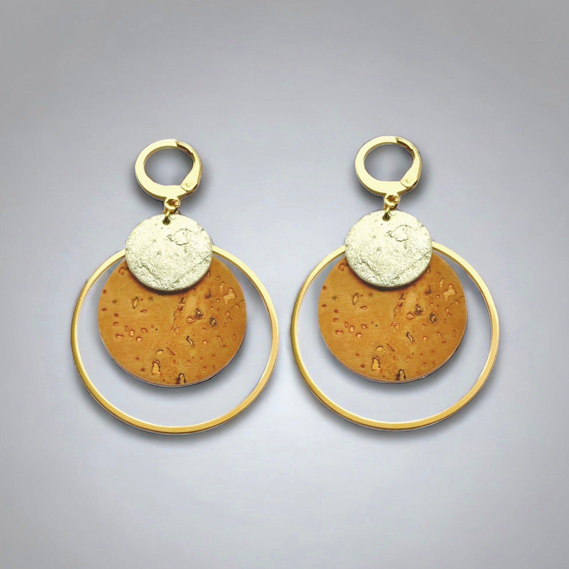 Boucles d'oreilles dorées rondes en liège brut et doré antique, soulignées par de grands anneaux dorés, sur fond gris