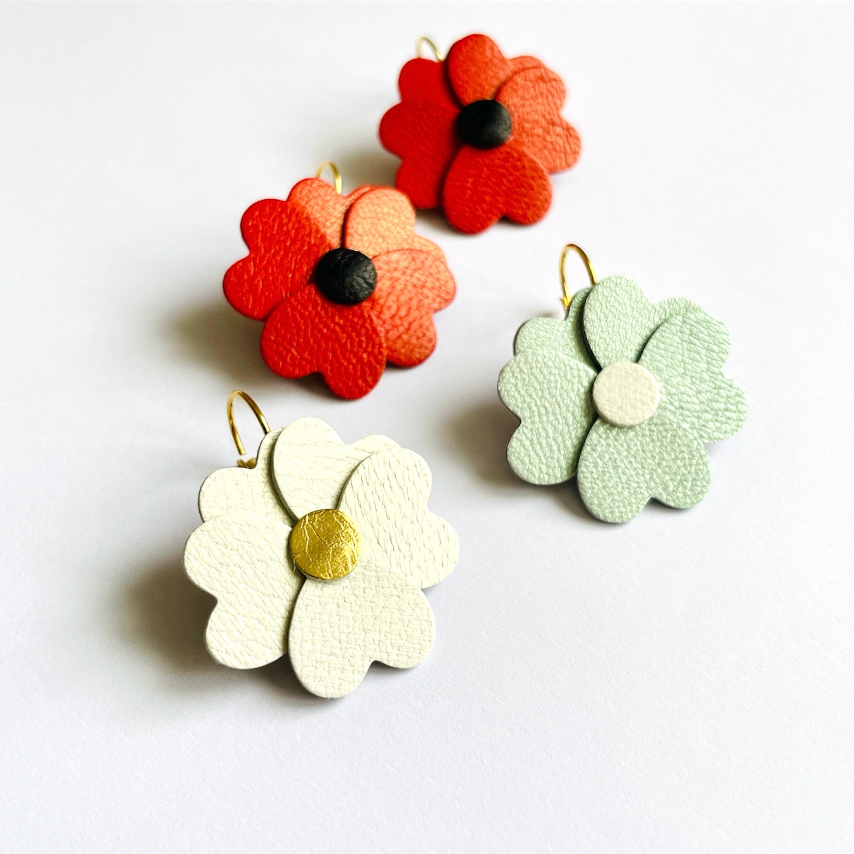 Boucles d'oreilles Nune en forme de petites fleurs , modèle Lalie, en cuirs coquelicot nacré & noir, blanc cassé nacré & doré, bleu lune nacré & blanc cassé nacré, sur fond blanc