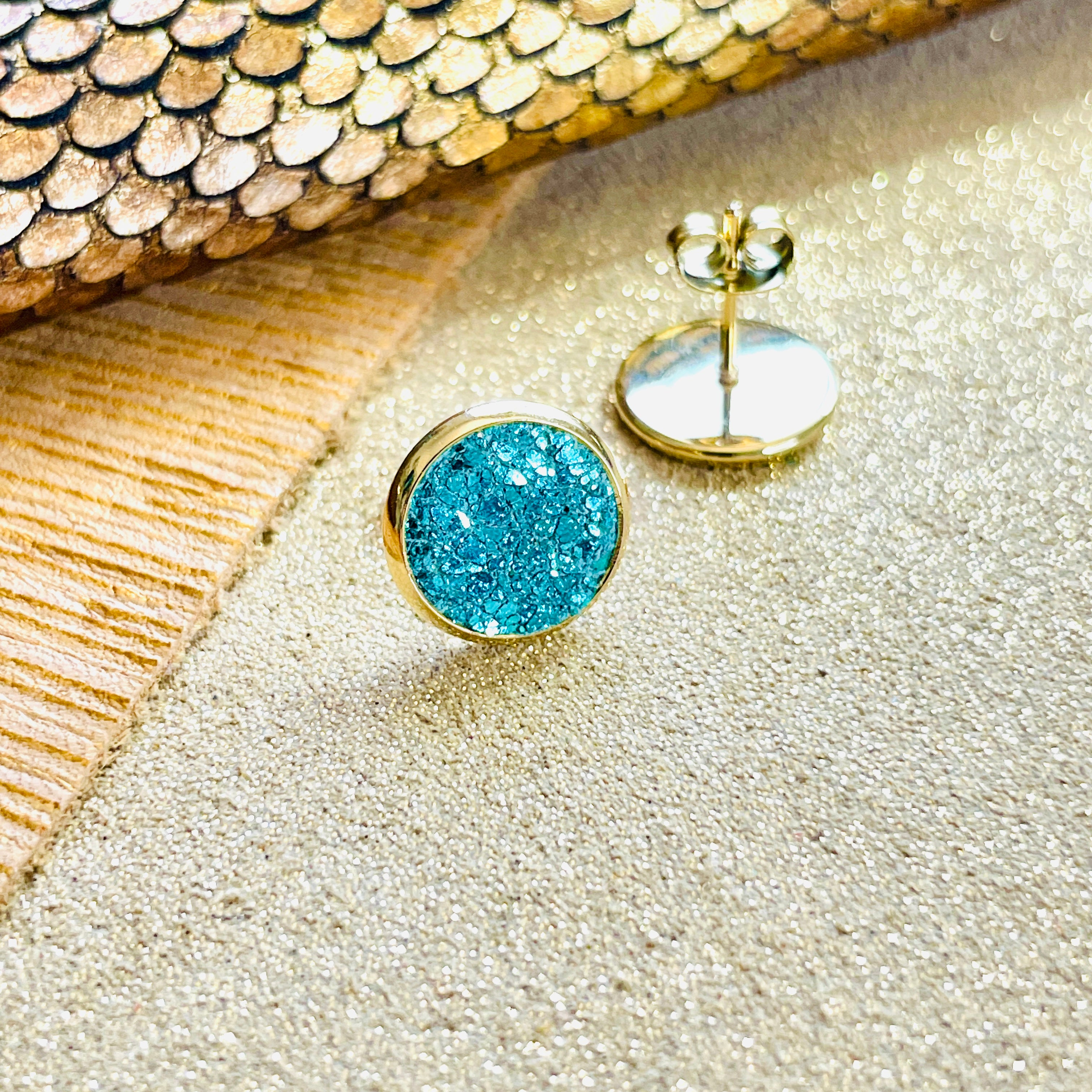 Puces d'oreilles dorées rondes Nune modèle Ilis avec cuir vert émeraude brillant intense, sur fond de cuirs beige