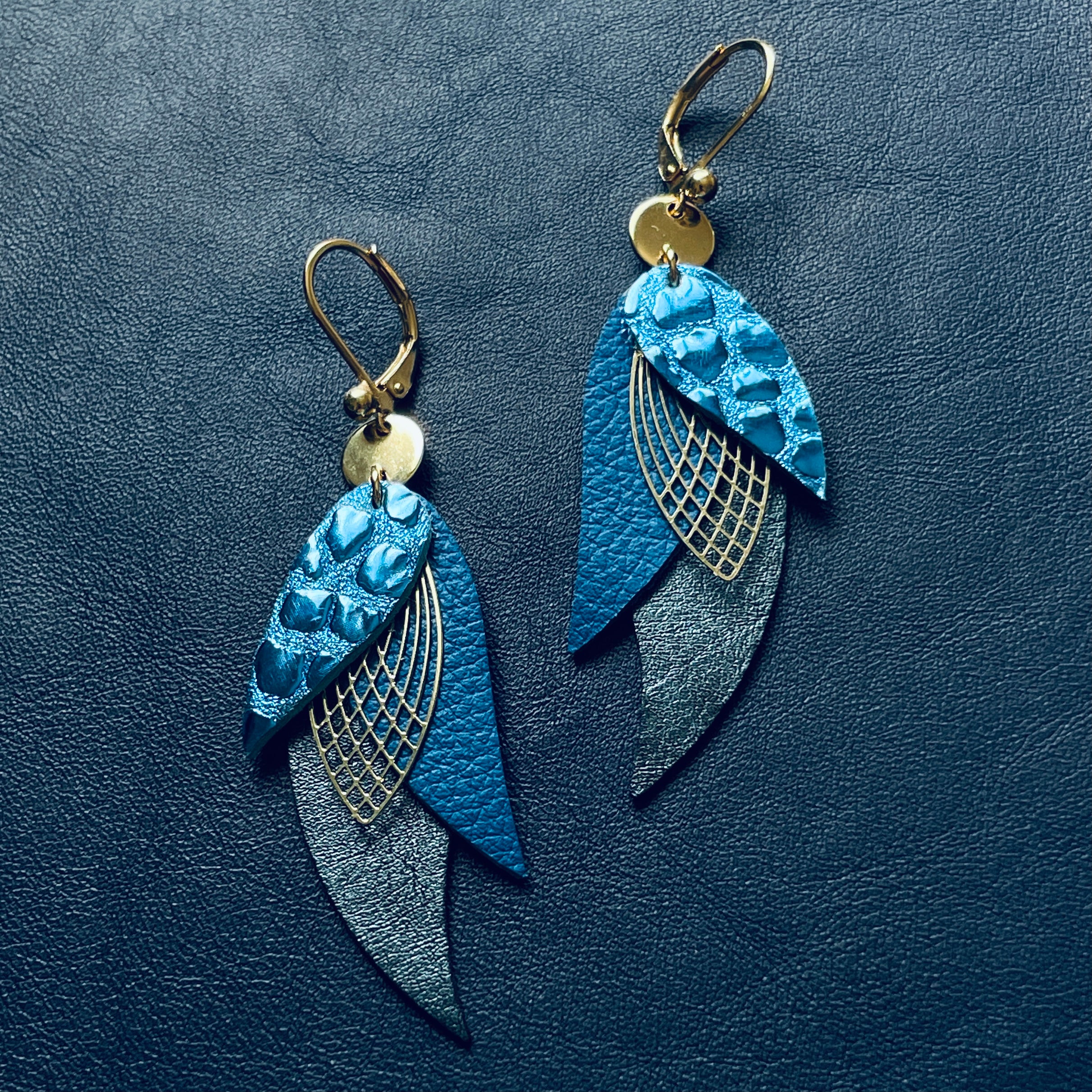 boucles d'oreilles dorées Nune modèle Ara en plumes de cuir bleu brillant façon croco, bleu marine grainé et bleu nuit métallisé sur cuir bleu marine