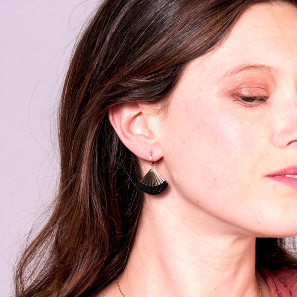Jeune femme vue de près portant les Boucles d'oreilles dorées Nune modèle Alya avec sequin éventail et pièces de cuir noir grainé irisé