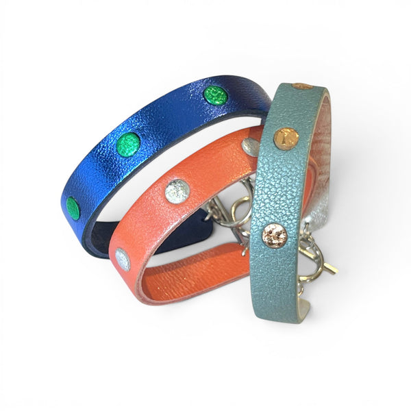 3 Bracelets argentés debout en cuirs bicolore bleu cobalt métallisé et vert métallisé, corail nacré et argent brillant froissé, et bleu gris nacré et or rosé froissé, empilés les uns sur les autres, sur fond blanc