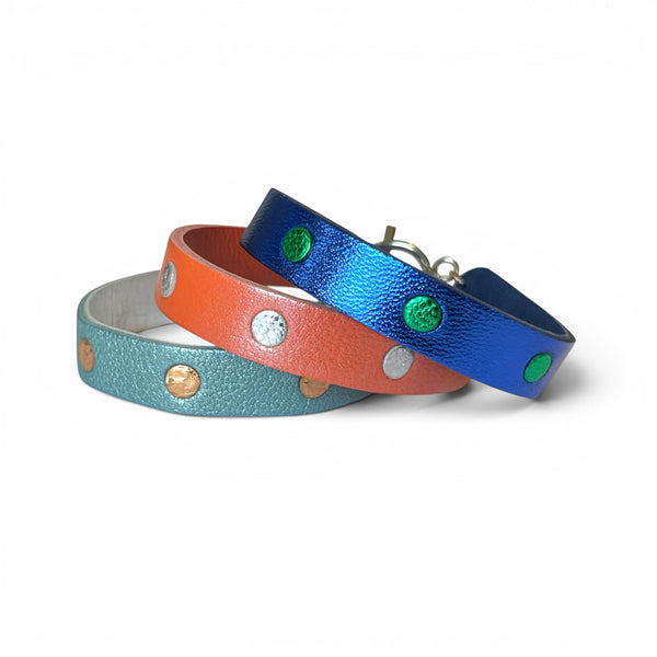 3 Bracelets argentés empilés en cuirs bicolore bleu cobalt métallisé et vert métallisé, corail nacré et argent brillant froissé, et bleu gris nacré et or rosé froissé, empilés les uns sur les autres, sur fond blanc