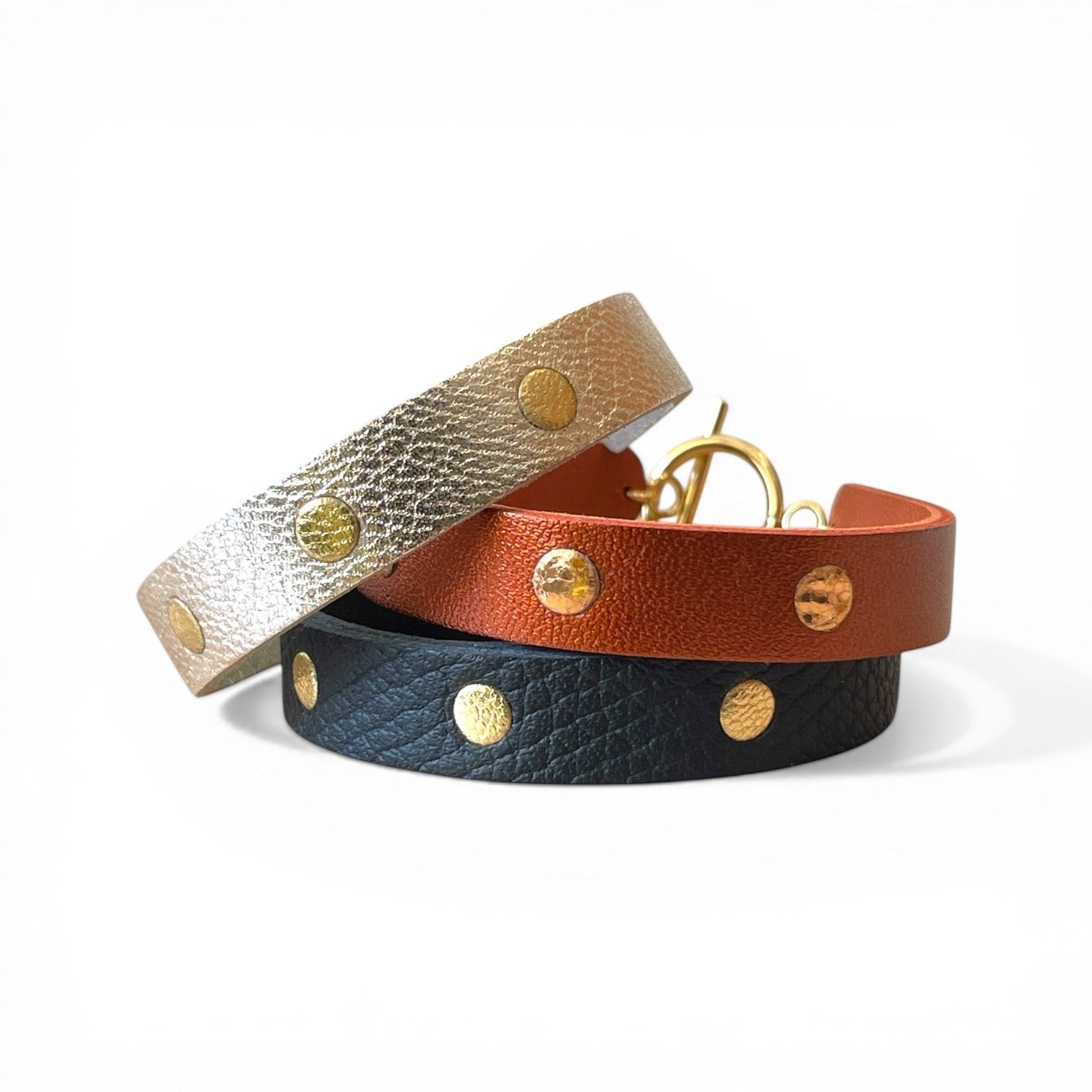 3 Bracelets dorés en cuirs bicolore argent et or, terracotta métallisé et or rosé froissé, et noir grainé et or, posés les uns sur les autres, sur fond blanc