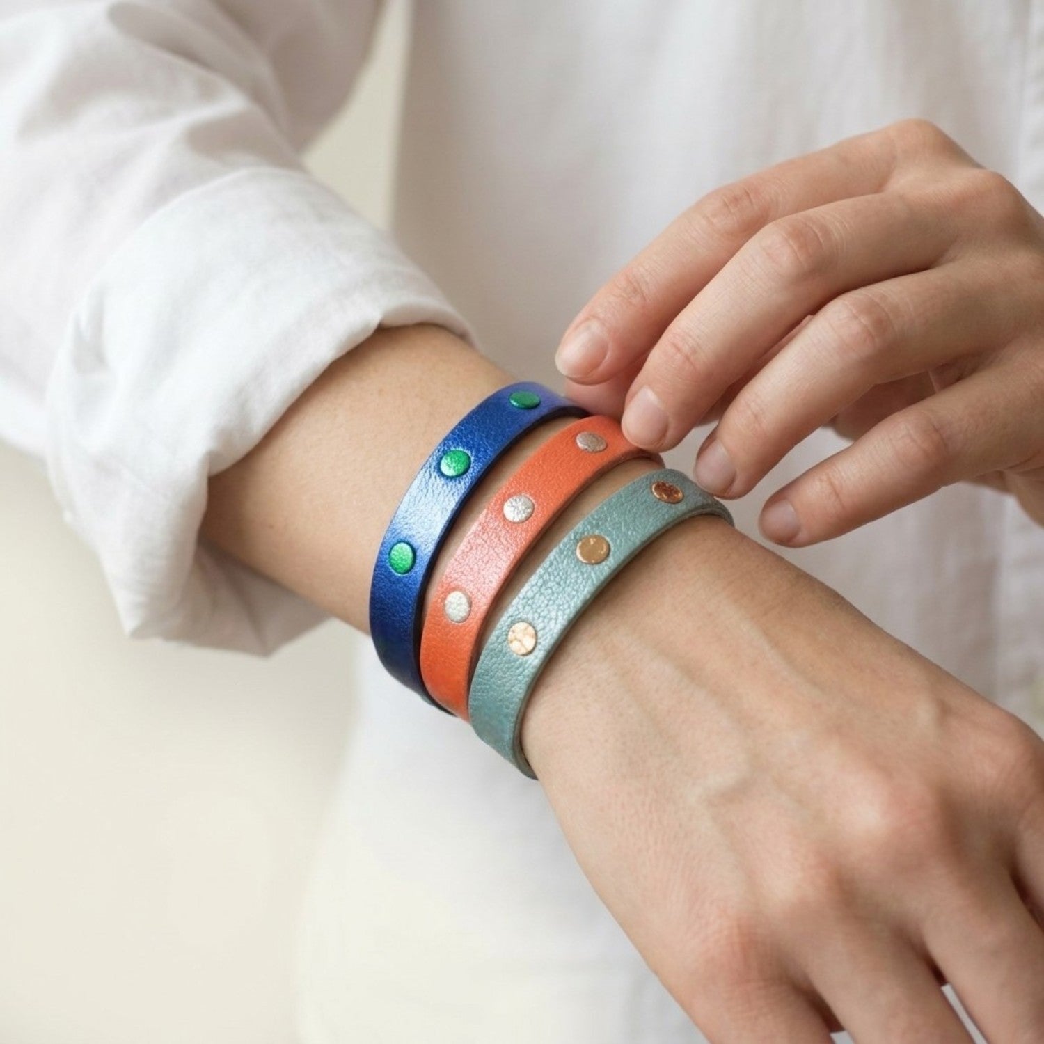 3 Bracelets argentés empilés en cuirs bicolore bleu cobalt métallisé et vert métallisé, corail nacré et argent brillant froissé, et bleu gris nacré et or rosé froissé, portés au poignet