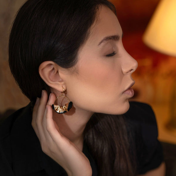 Grandes boucles d'oreilles dorées en froufrous de cuir recyclé bicolore noir et doré, portées à l'oreille par une femme brune