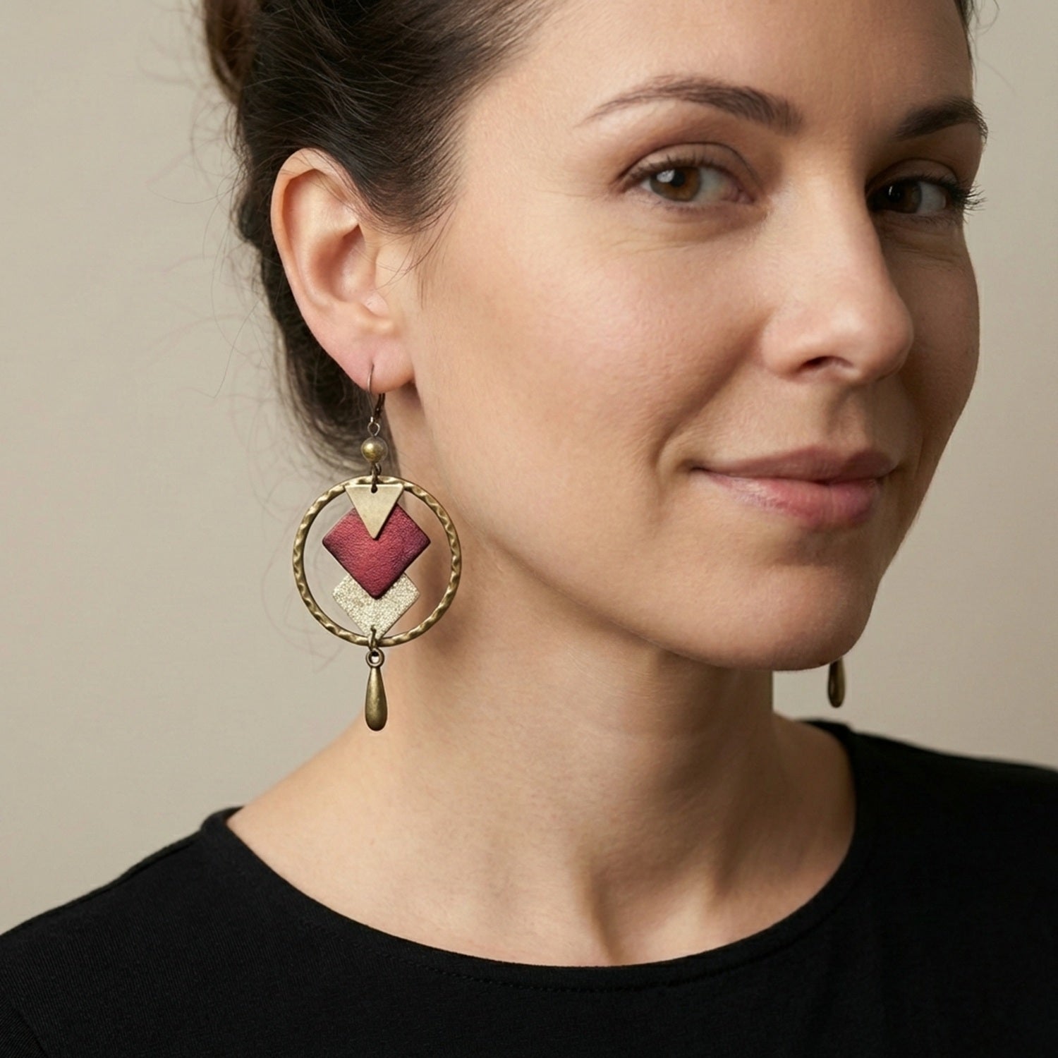 Boucles d'oreille en bronze Nune modèle Adamante Créoles en cuir grenat métallisé portées aux oreilles par une femme brune