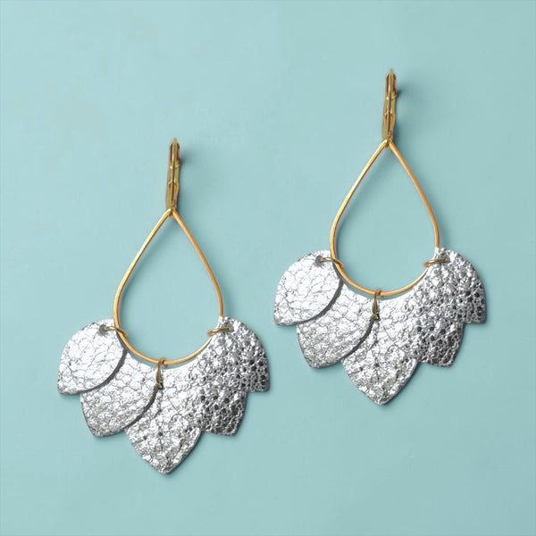 Boucles d'oreilles Nune modèle Aponi dorées à l'or fin avec pétales de cuir argent brillant froissé, sur fond vert