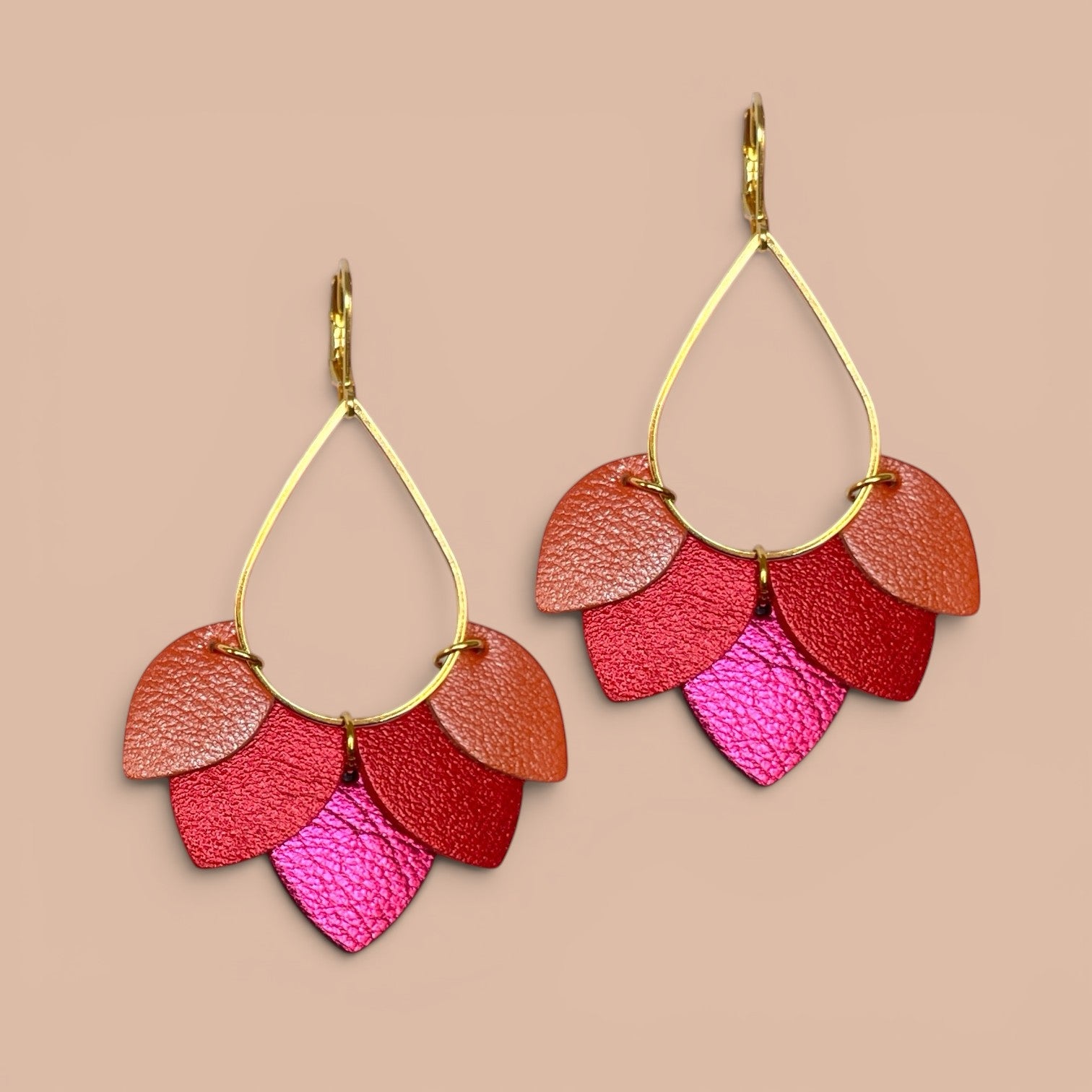 Boucles d'oreilles Nune modèle Aponi dorées à l'or fin avec pétales de cuirs corail nacré, coquelicot nacré et fushia métallisé, sur fond beige rosé